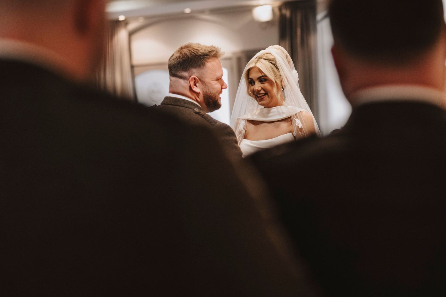 A couple in wedding attire shares an intimate moment during their ceremony at an indoor venue.