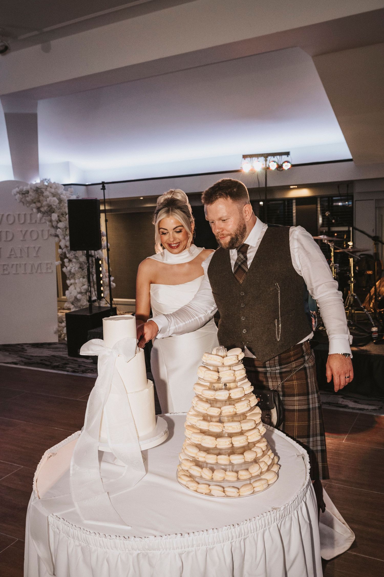 A couple cuts their tiered macaron wedding cake display at their elegant reception celebration.