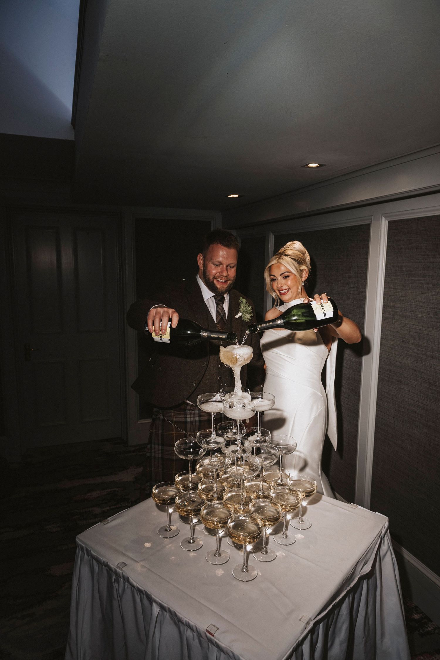 A wedding couple pours champagne into a tower of stacked glasses creating an elegant cascading effect at their reception.