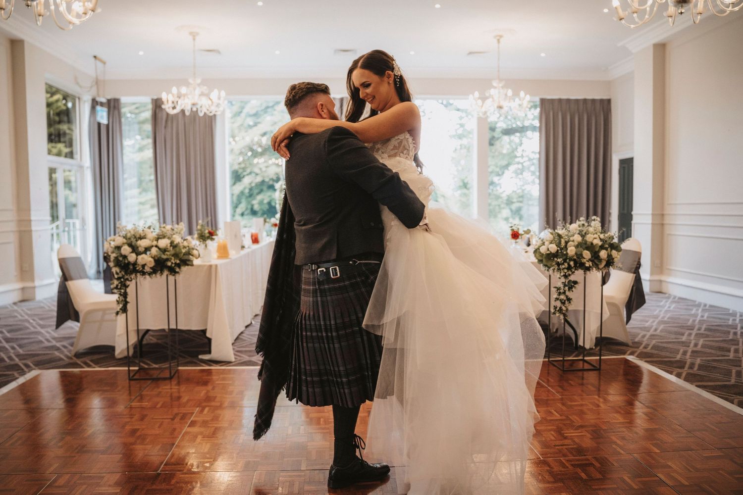 A romantic wedding couple dancing in an elegant ballroom with crystal chandeliers overhead.