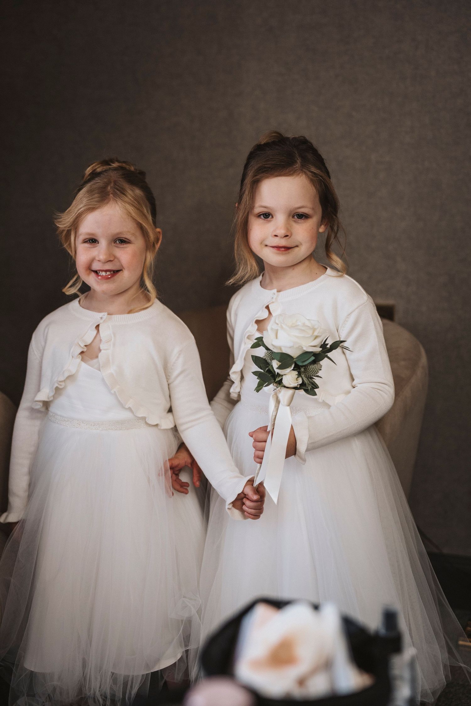 Two children in matching white dresses and cardigans share playful moments in a series of formal portrait photos.