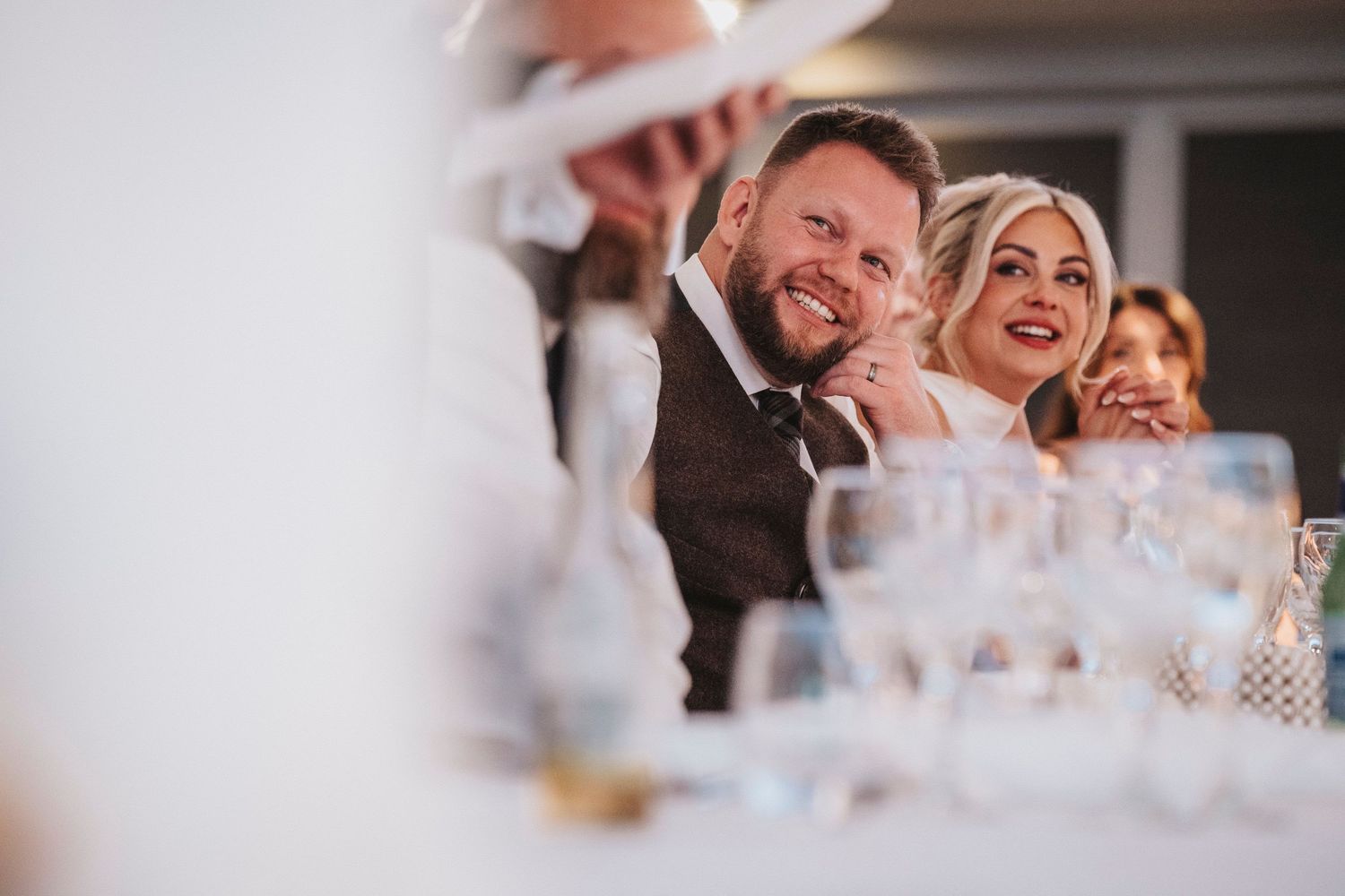 A couple shares a joyful laugh together at a formal event with wine glasses visible in the background.