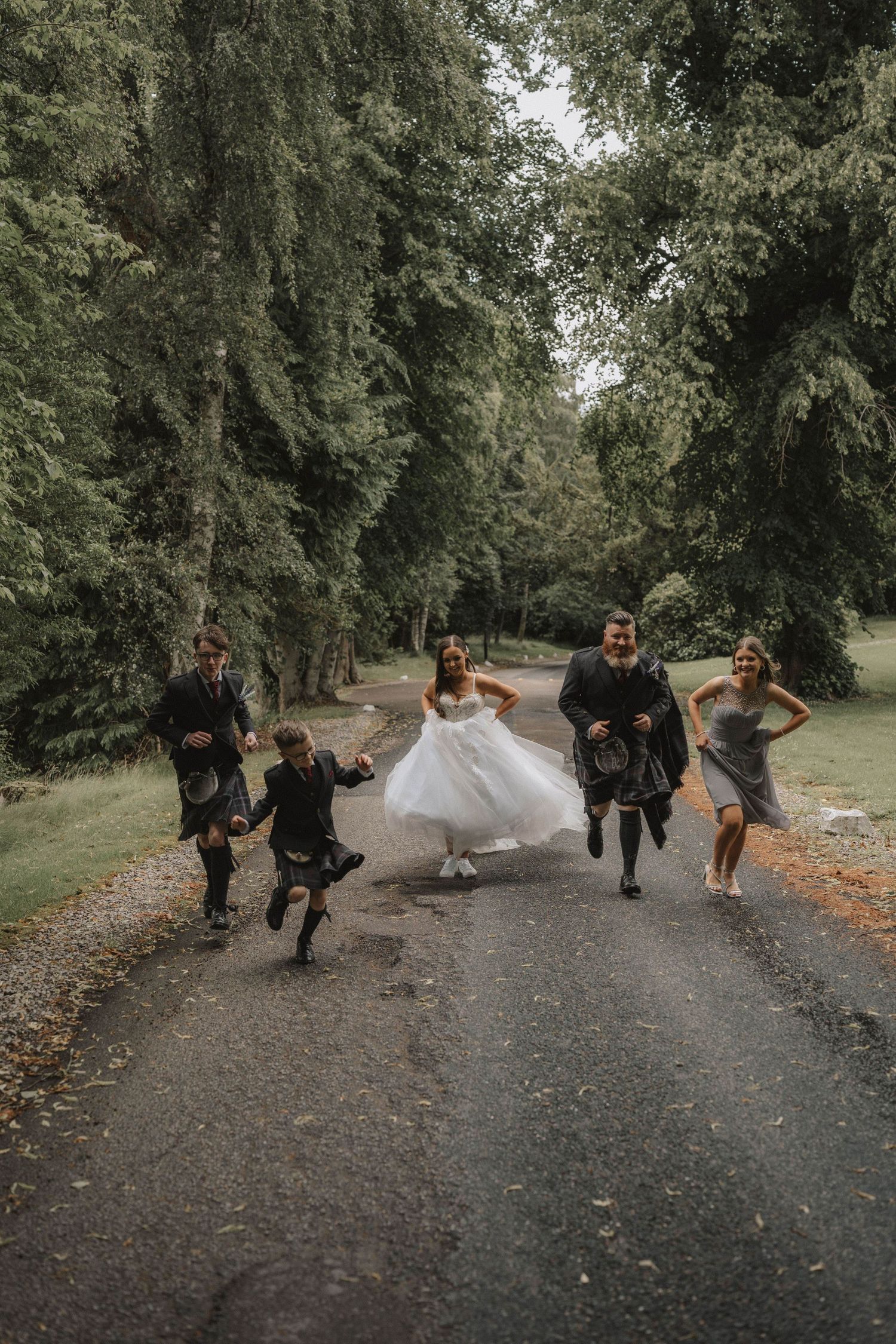 Wedding party runs playfully down a wooded path while celebrating.