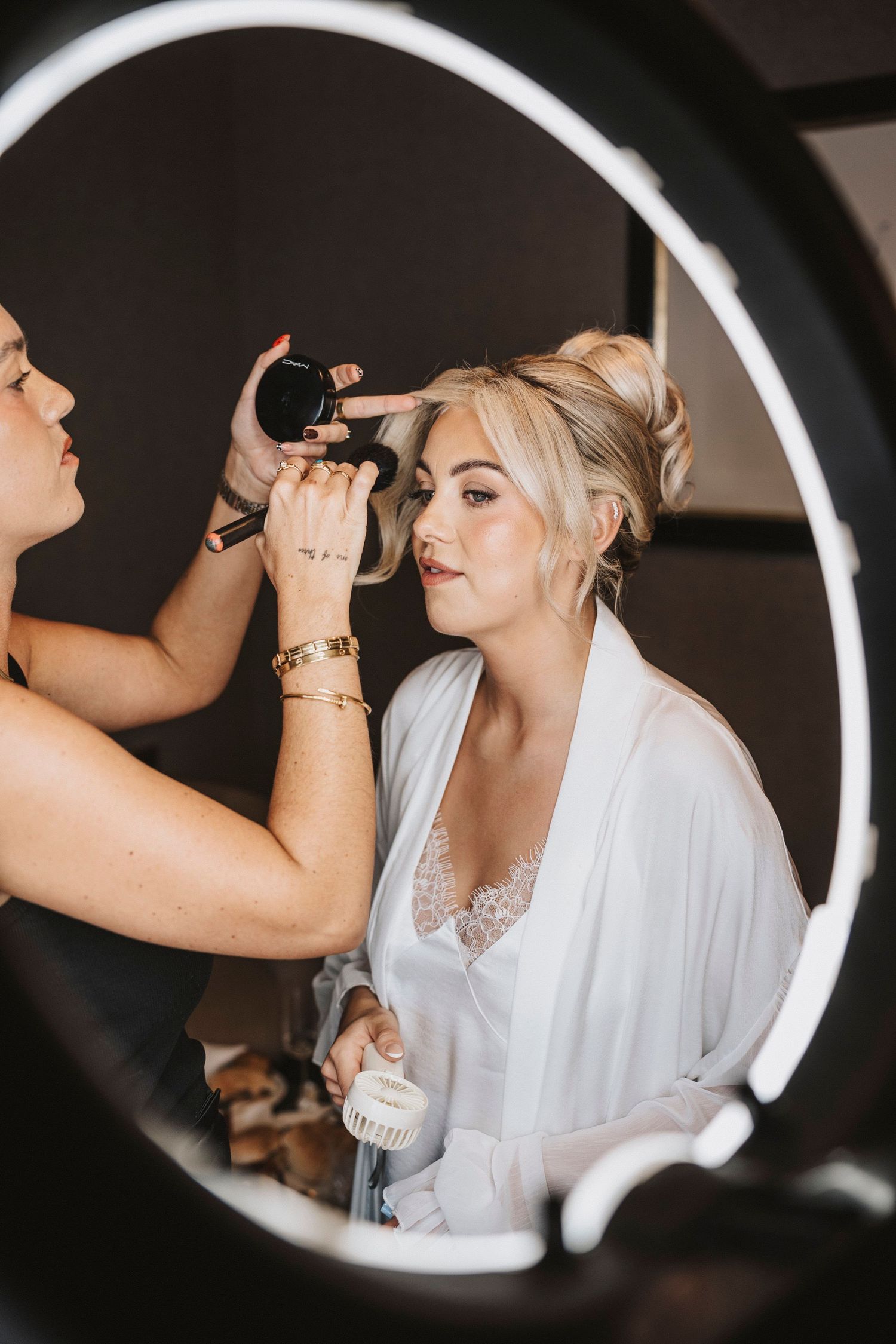 Behind-the-scenes wedding preparation showing makeup application in a circular ring light reflection.
