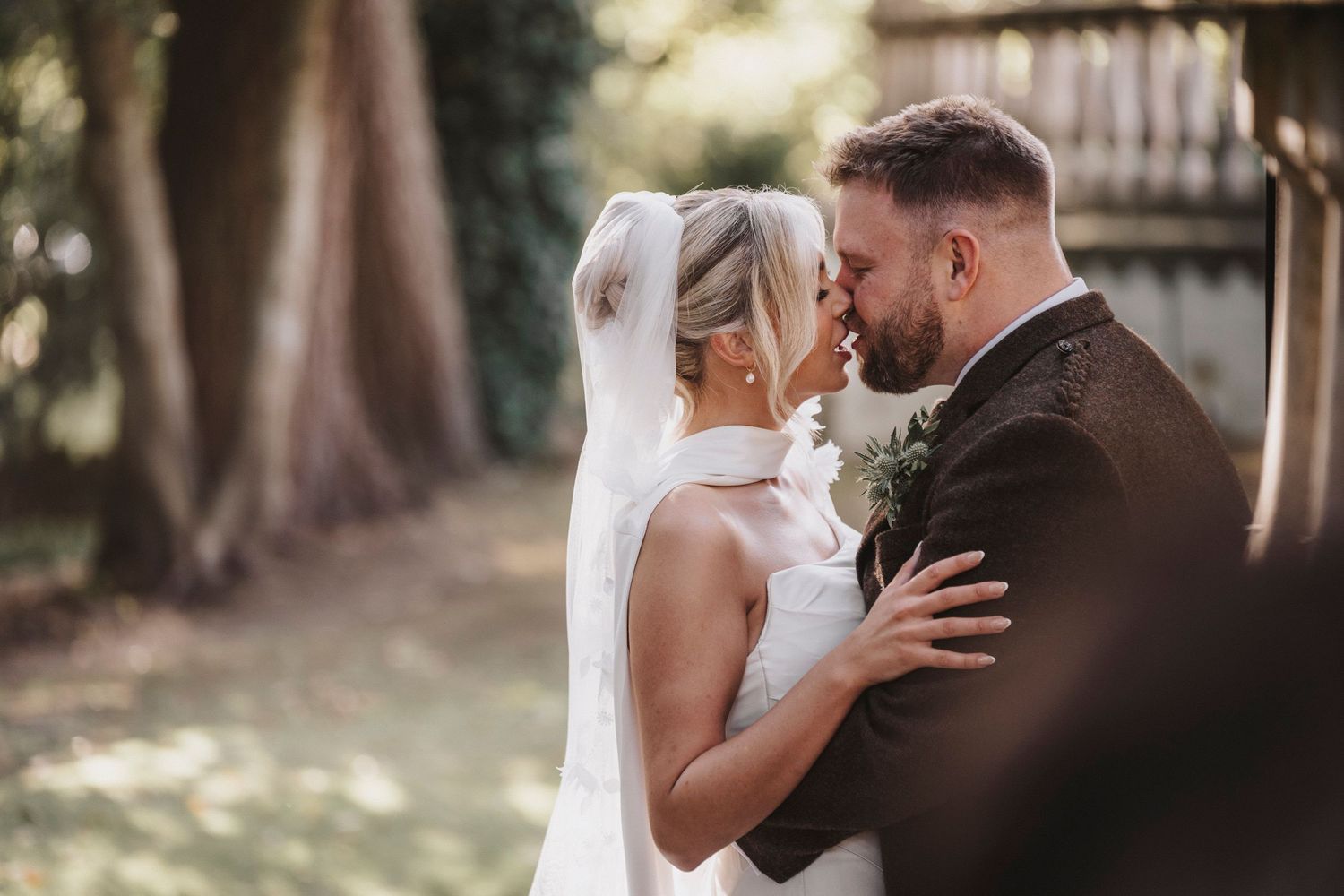 A romantic wedding moment captured outdoors with a couple embracing in soft natural lighting.