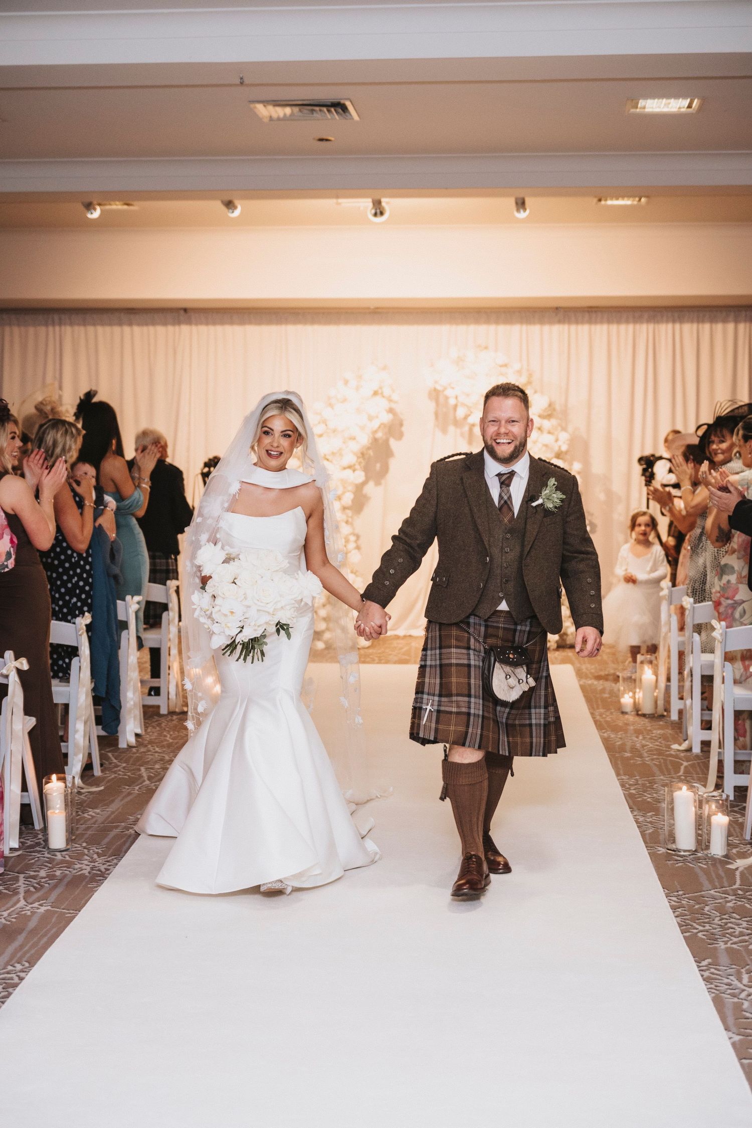 Newlyweds make their grand exit through a wedding venue lined with guests throwing confetti and rose petals.
