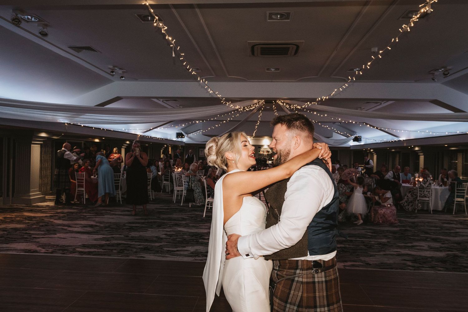 Couple dancing together at an elegant wedding reception venue decorated with twinkling lights.