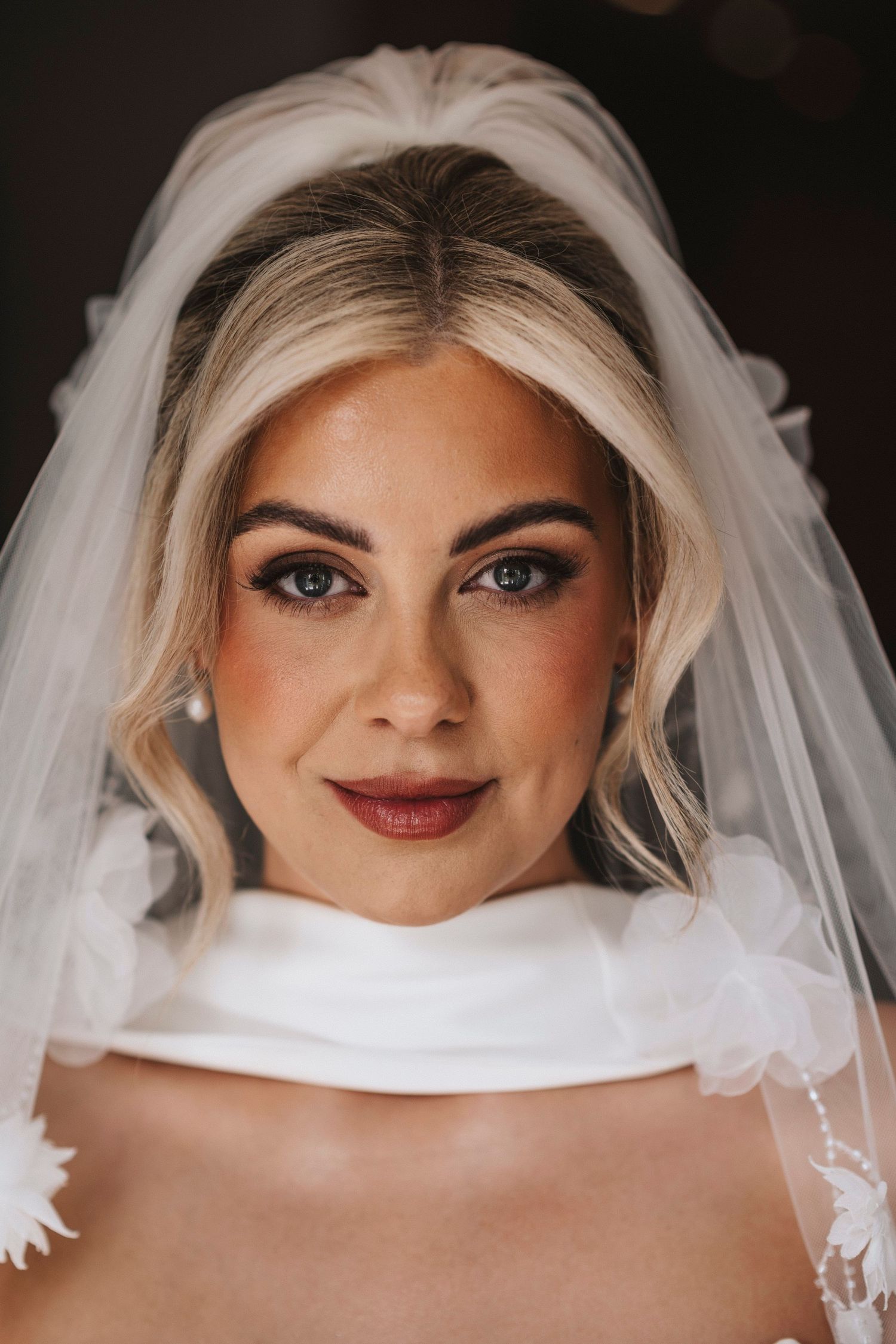 Close up portrait shots of a bride wearing a white veil and burgundy lipstick in different poses.