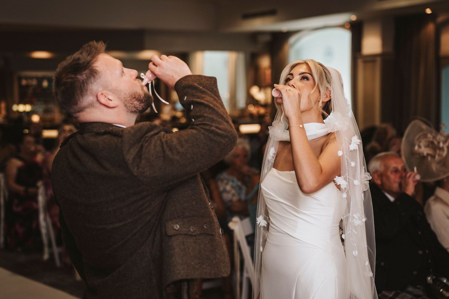 A couple shares a romantic dance at an elegant wedding reception with warm lighting and guests in the background.