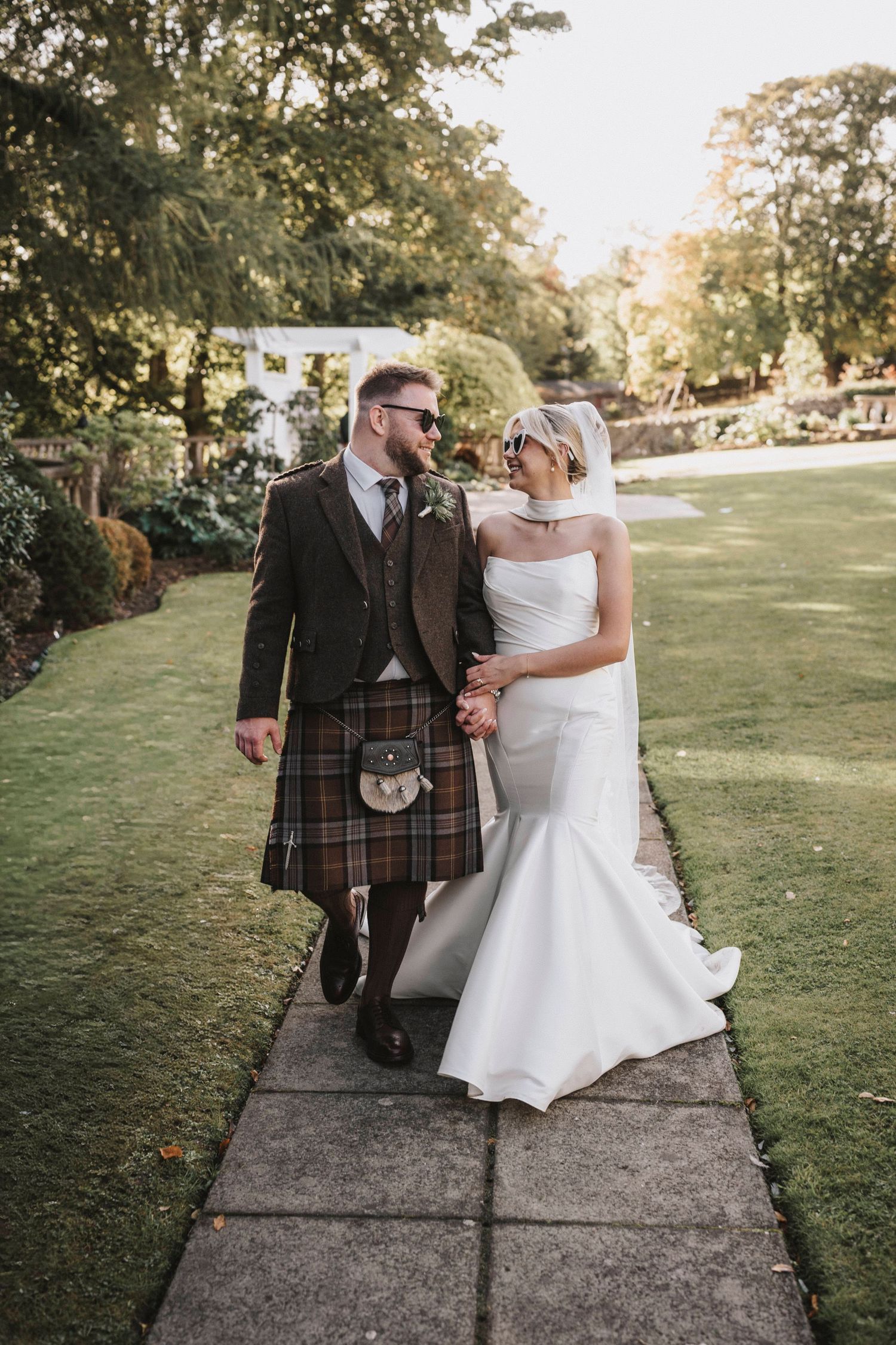 A couple in wedding attire walks along a stone path surrounded by lush greenery on their special day.