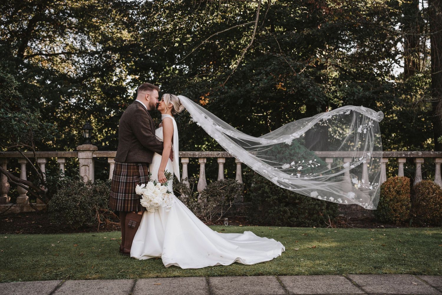 A flowing white wedding veil catches the breeze in a romantic outdoor garden setting during a summer photoshoot.