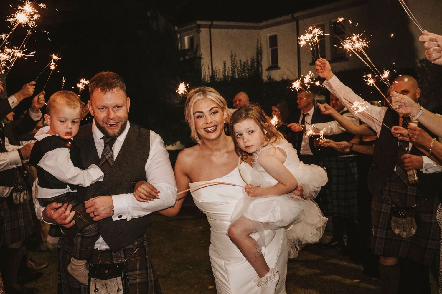 Wedding guests hold sparklers creating a magical nighttime tunnel for the newlyweds during their reception celebration.