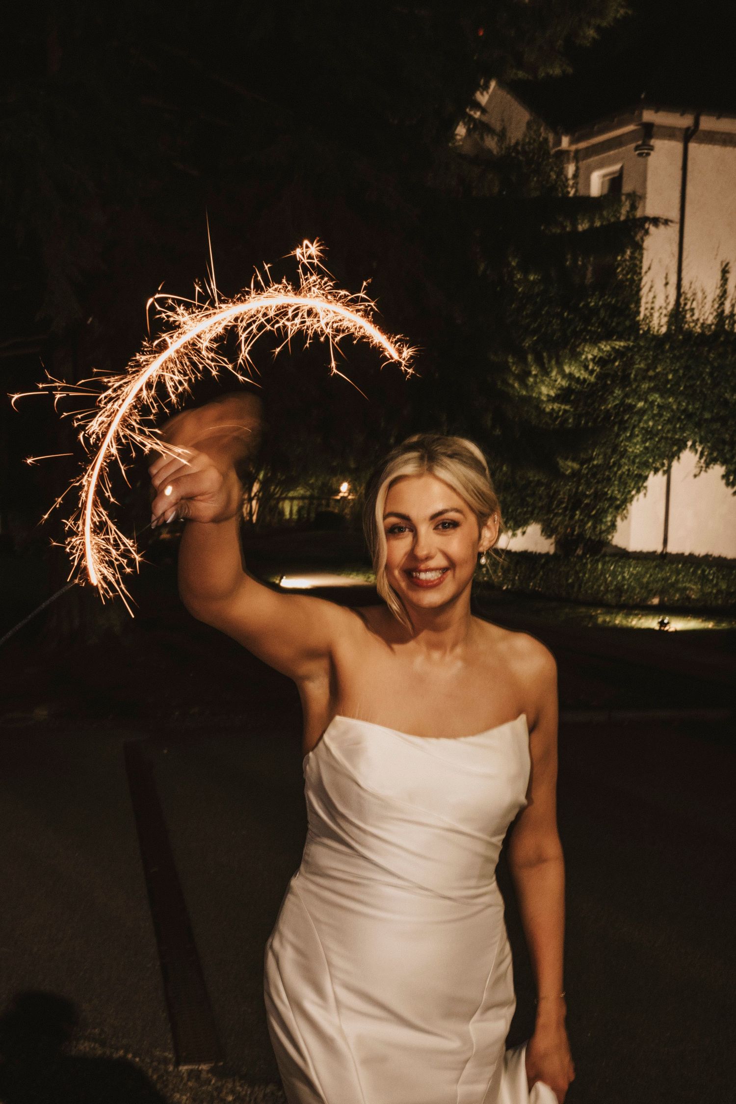 A joyful sparkler moment captured at a nighttime wedding celebration in an elegant white gown.