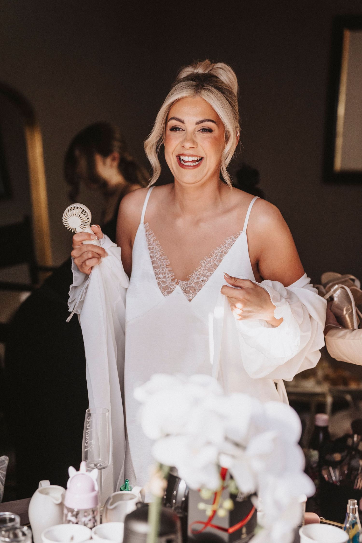 A bride in a white wedding dress laughs joyfully during an indoor wedding reception celebration.