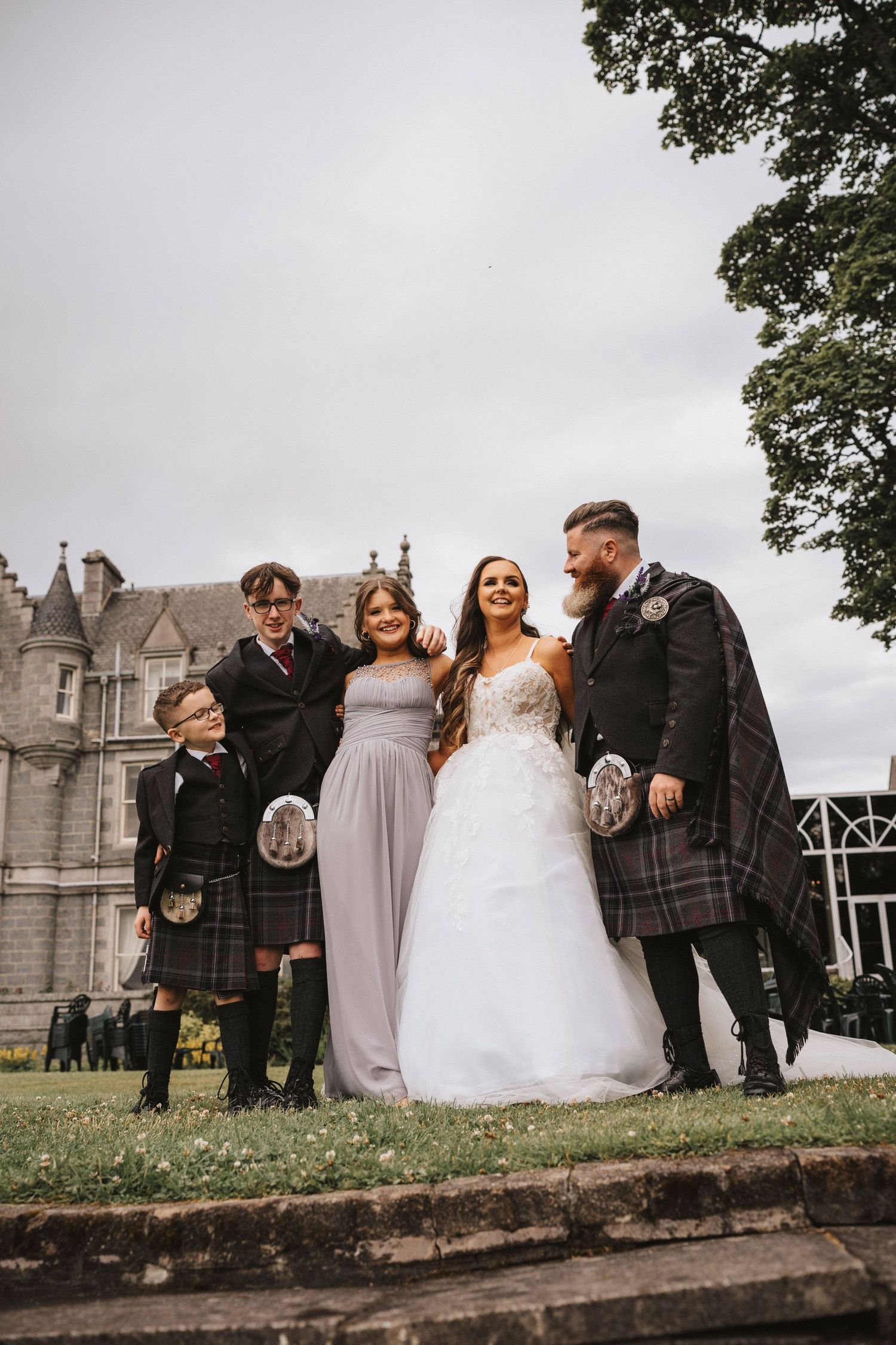 Wedding party stands together on stone wall with castle architecture in background.