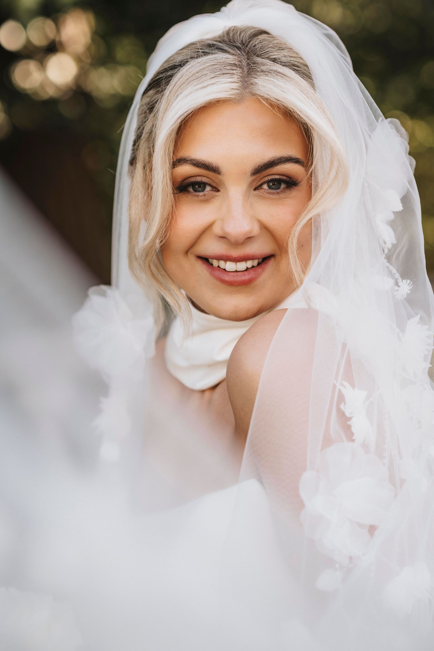 Close-up portrait of a bride wearing a delicate white veil and elegant makeup in natural lighting.