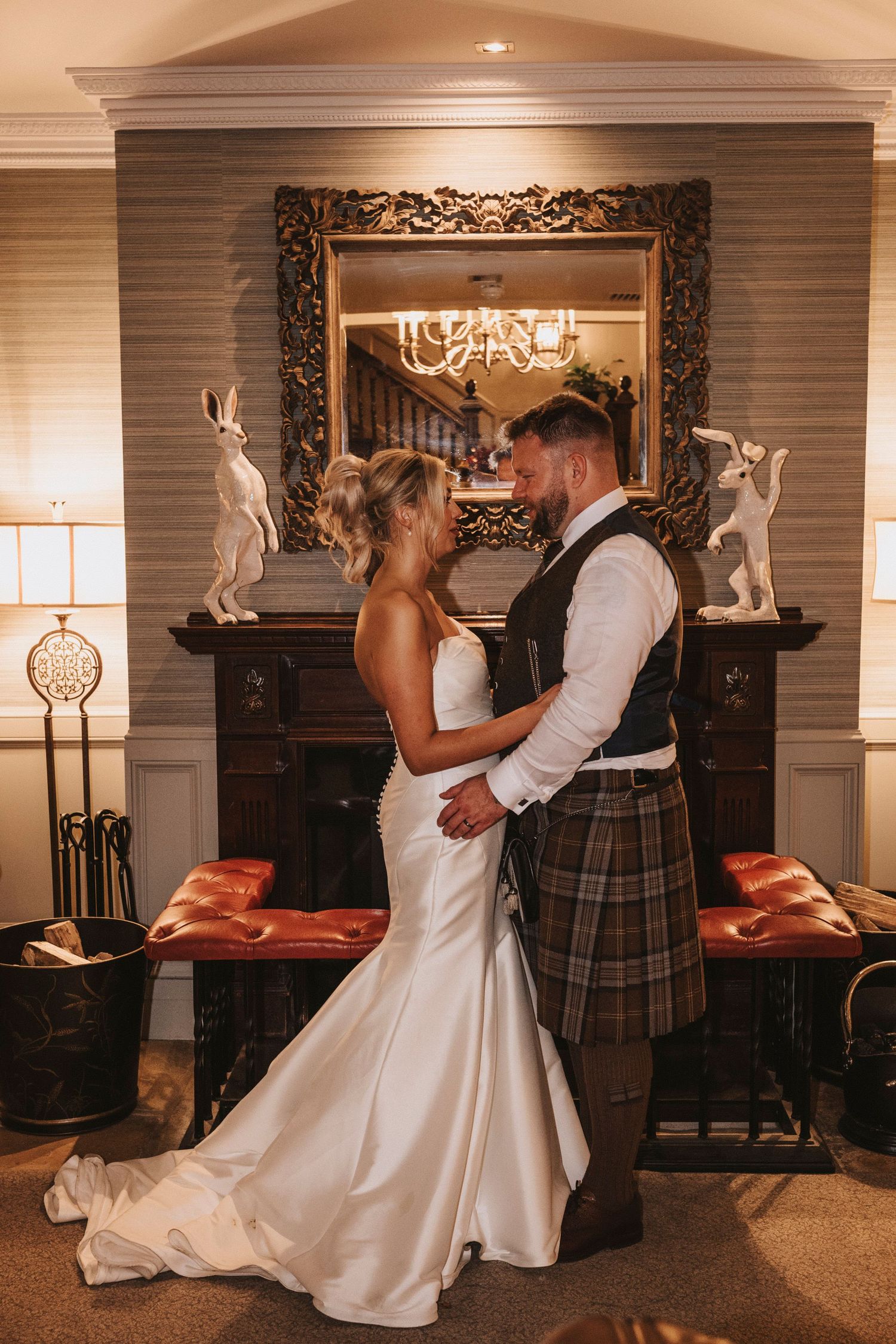A romantic wedding couple dances together in an elegantly decorated indoor venue with warm lighting and ornate decor.