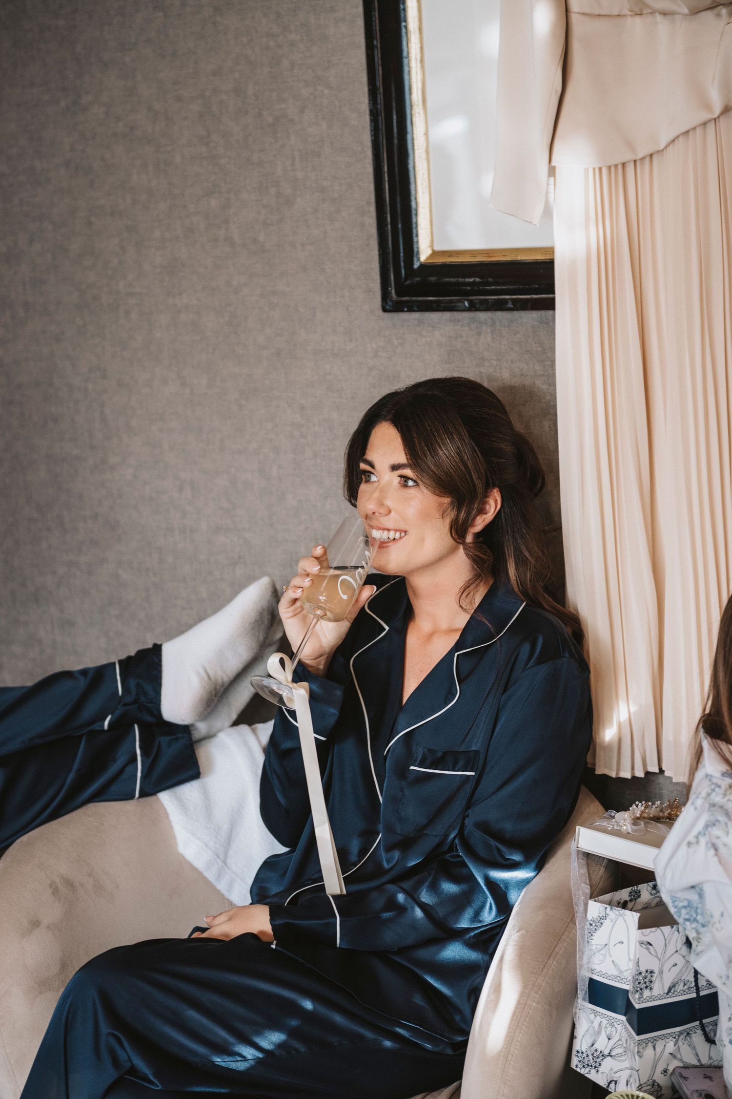 A series of photos showing someone in navy silk pajamas lounging on white bedding while holding a drink.