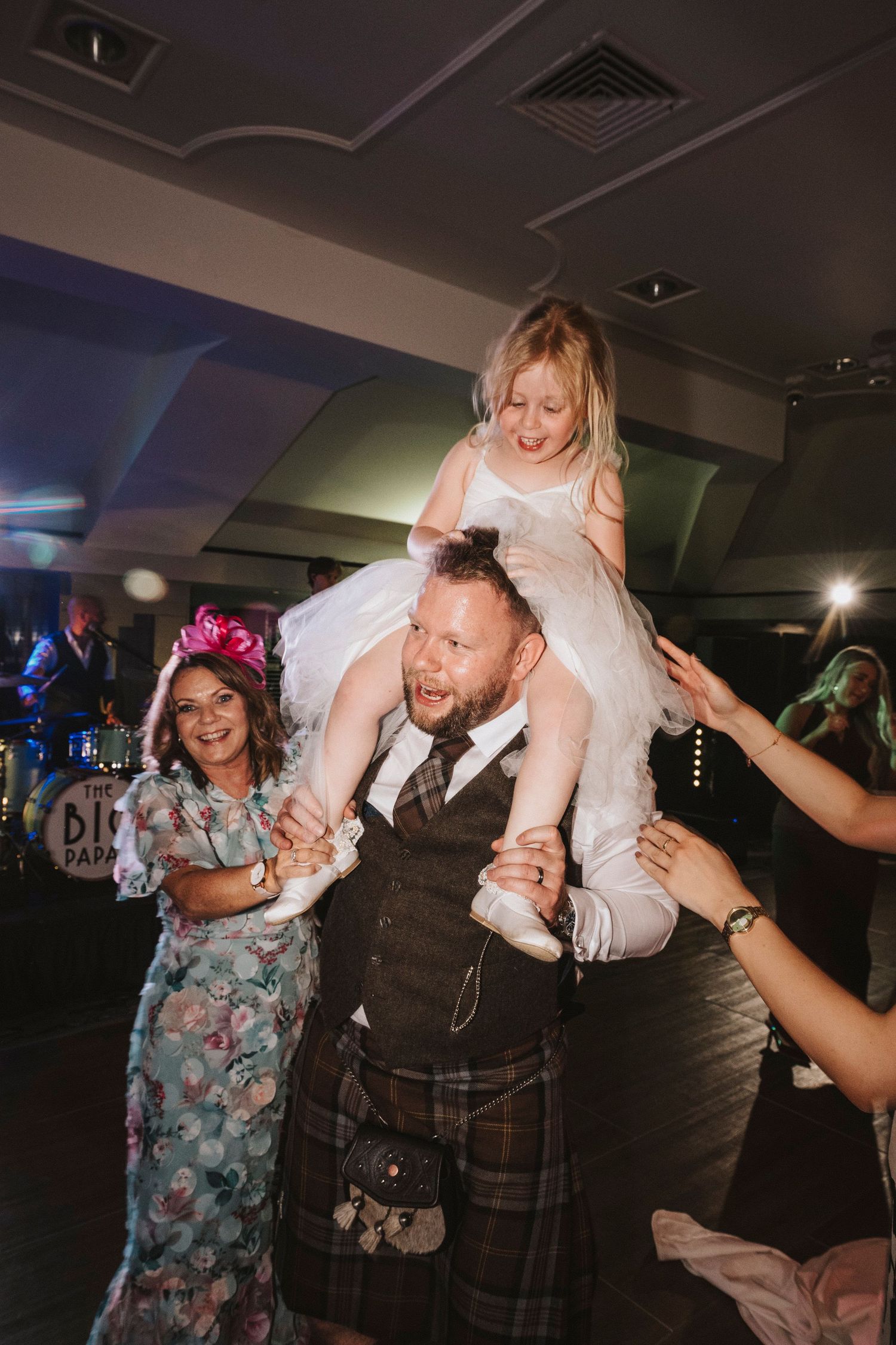 Wedding guests dance and celebrate during a lively reception with the bride and groom in traditional Scottish attire.