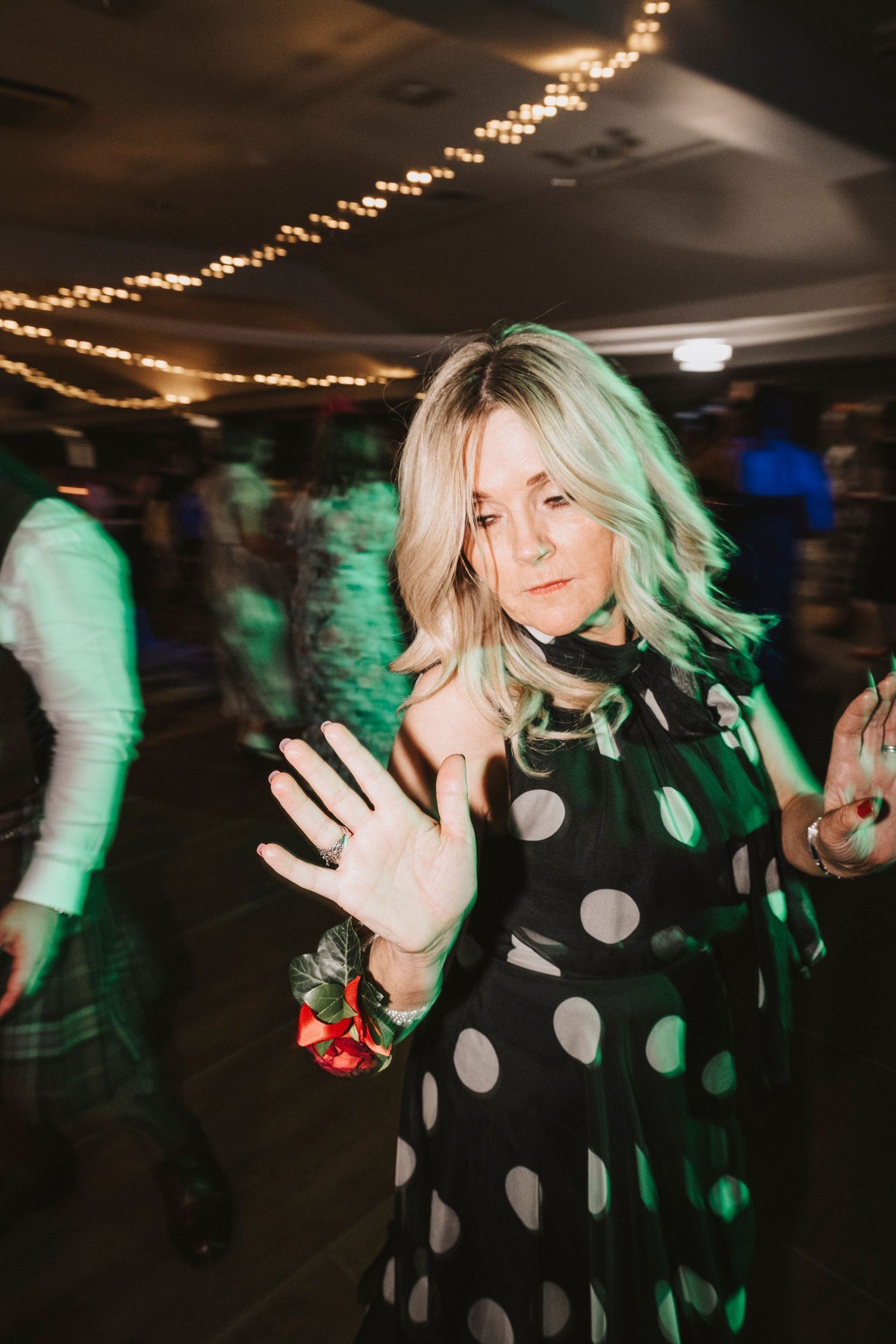 Motion blur captures dancing at a party with string lights overhead and green lighting creating an energetic nightclub atmosphere.