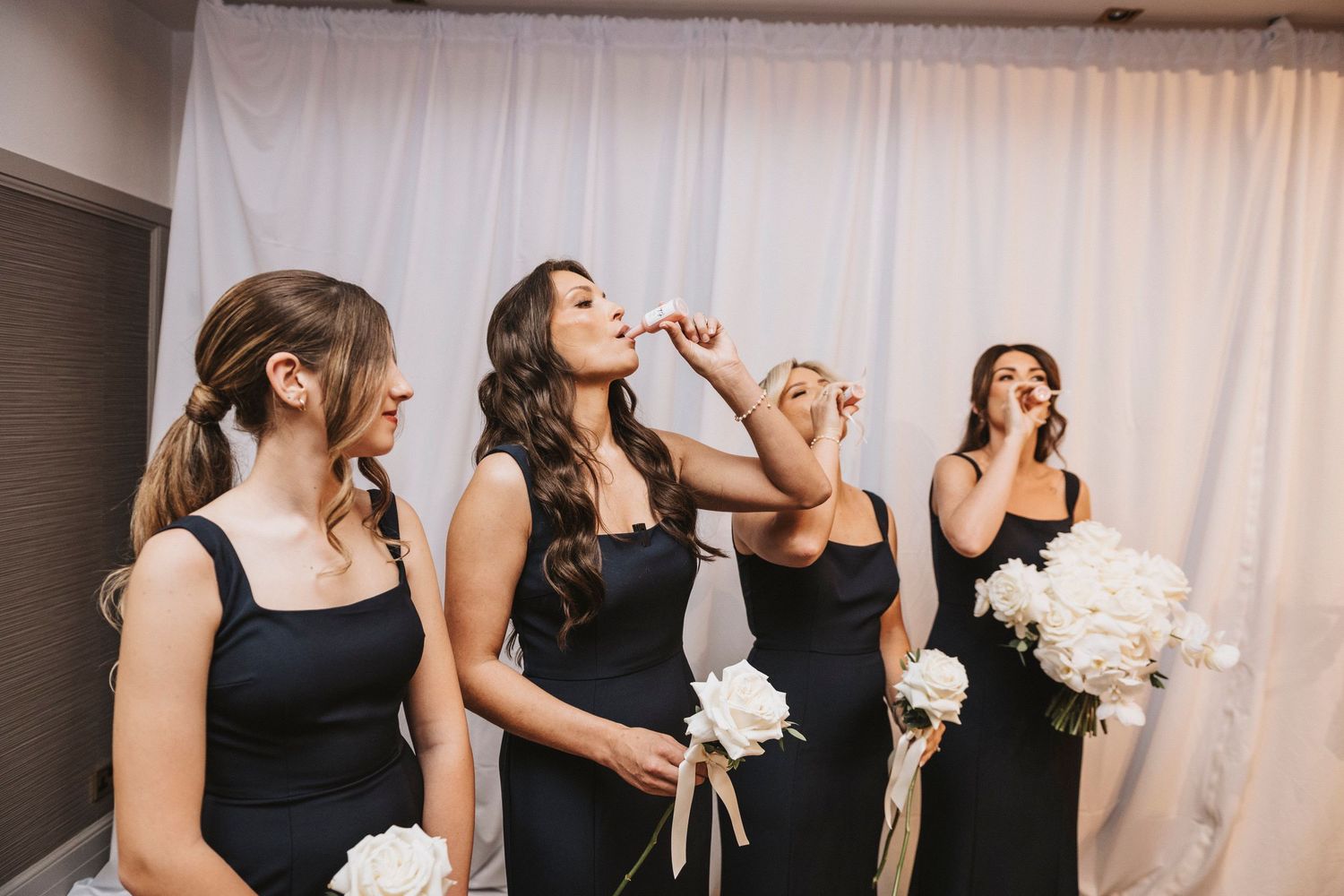A group of bridesmaids in black dresses share a champagne toast during a wedding celebration.