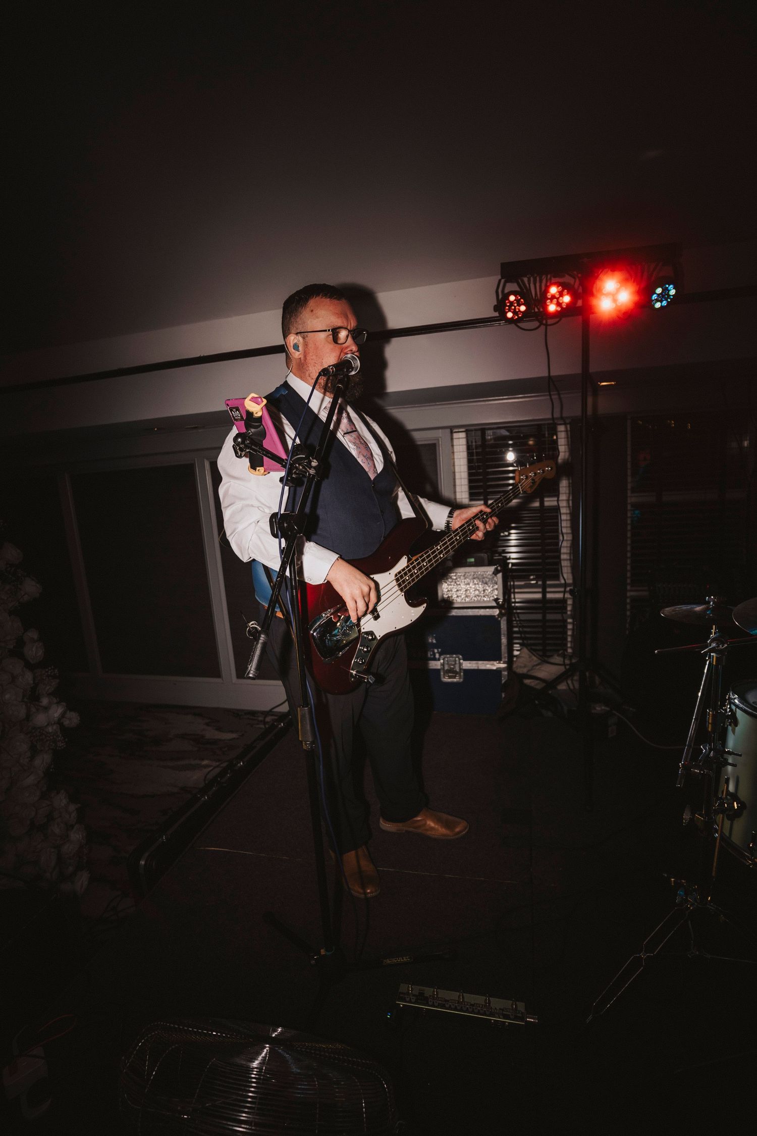 A musician performs on stage with an electric guitar in dark lighting with red stage lights glowing in the background.
