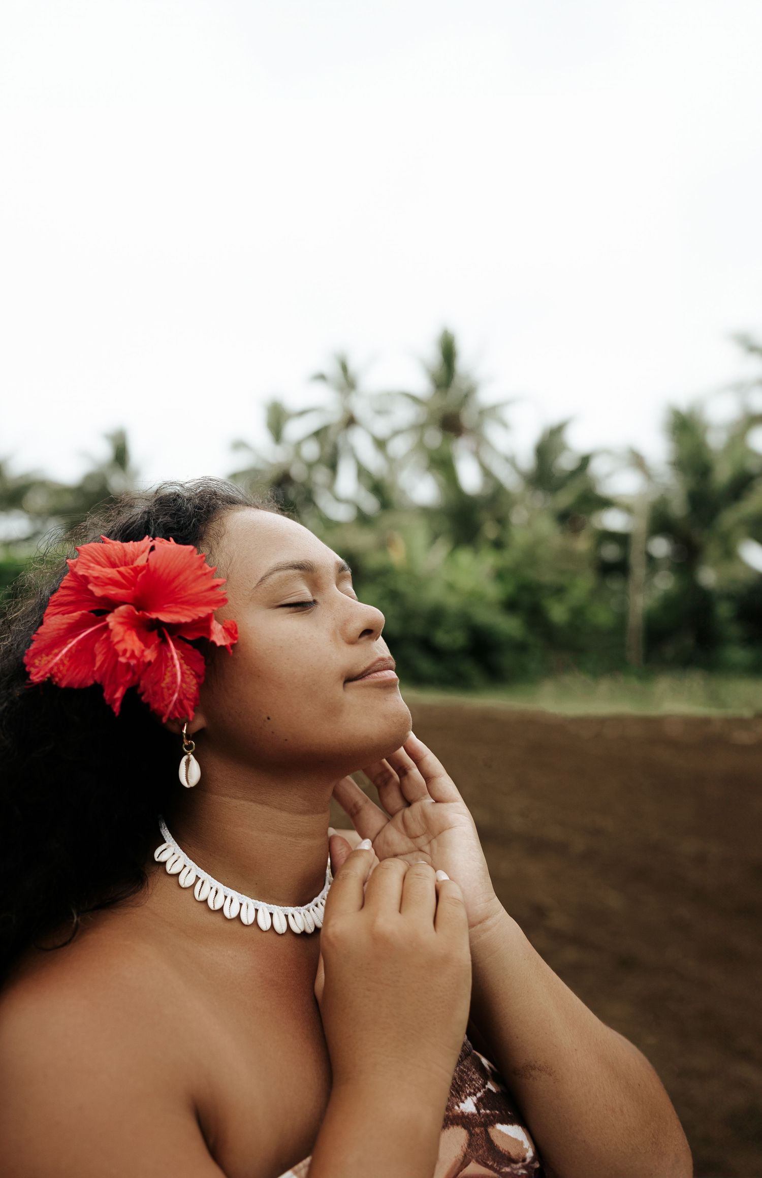 Woman with red hibiscus behind her ear looking up peacefully – Cook Islands creative portrait Coconut trees in the background