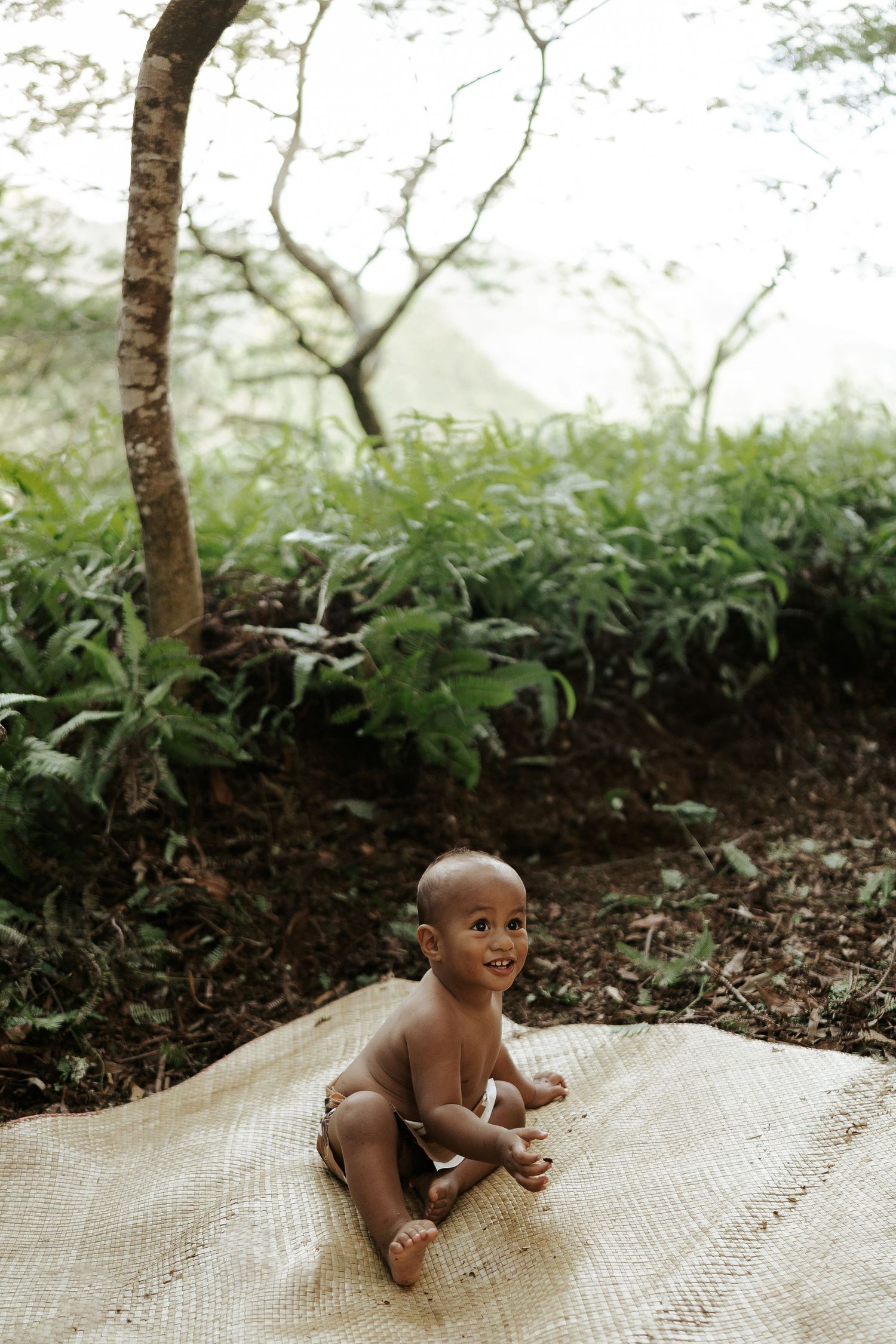 Little Boy sitting on a mat n the Lush Rarotonga Bush-smiling