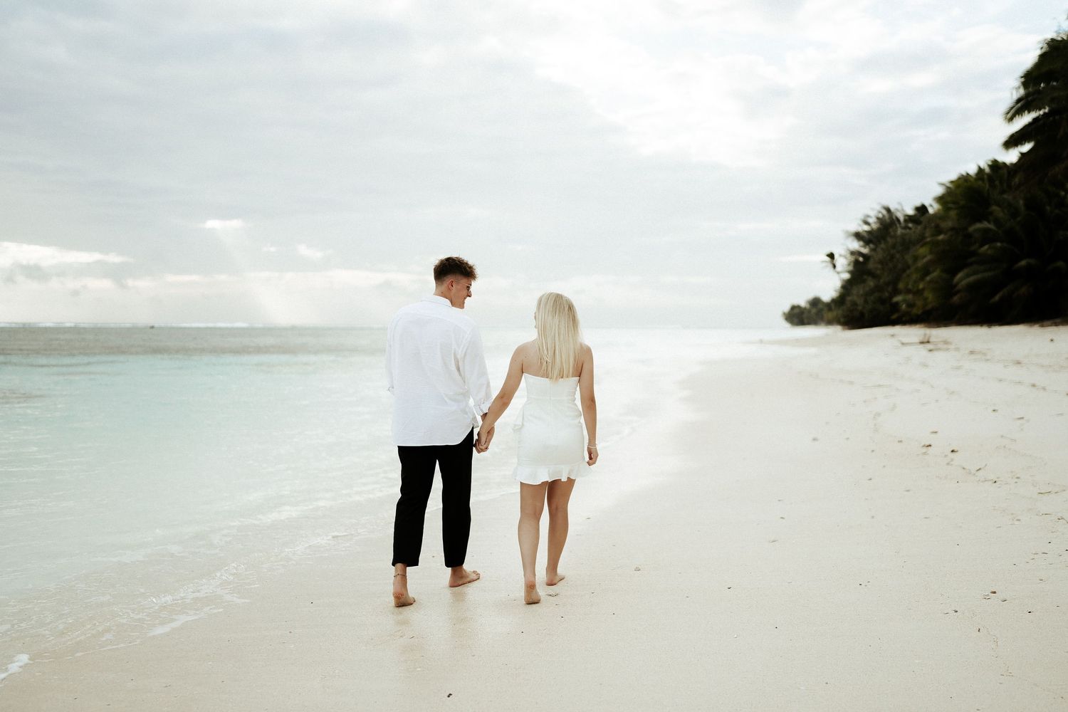 Couple walking away on beach, backs to camera – candid moment at sunset, Cook Islands