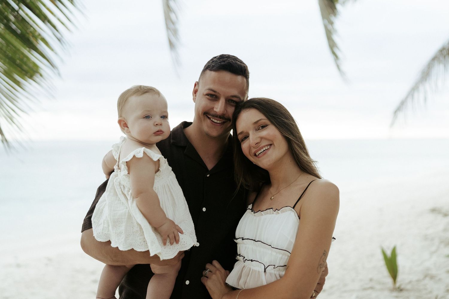 Family of three smiling on beach with baby in arms – joyful family session in Rarotonga