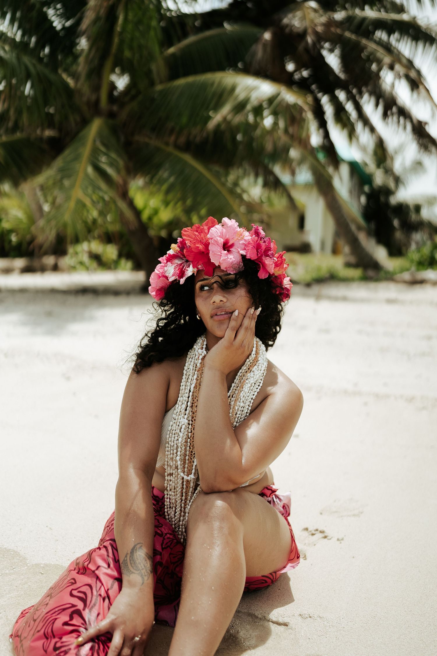 Woman in pink floral pareu sitting on the sand smiling – relaxed beach portrait in Rarotonga