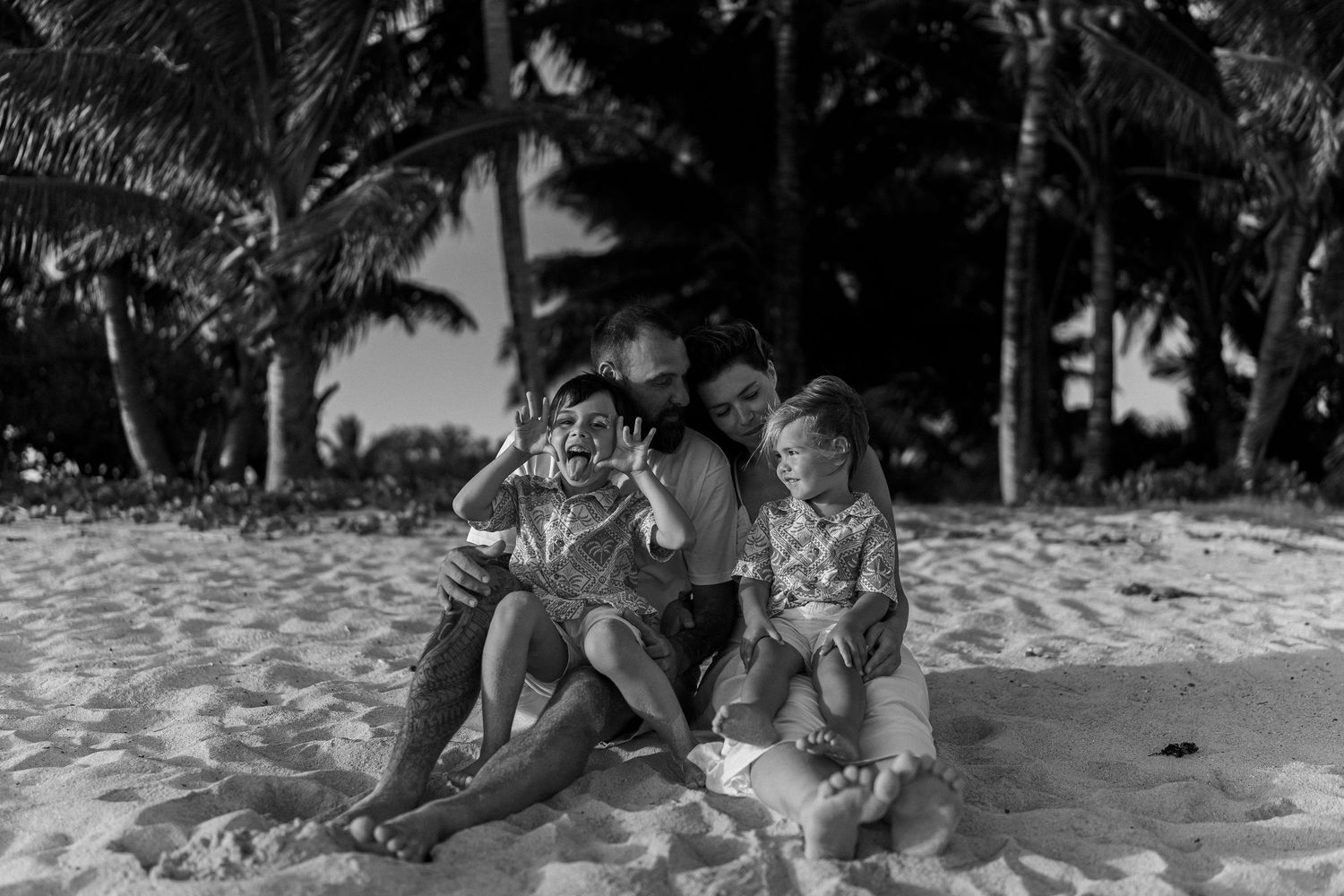 Couple cuddling their two boys on the beach in black and white – intimate moment in the Cook Islands