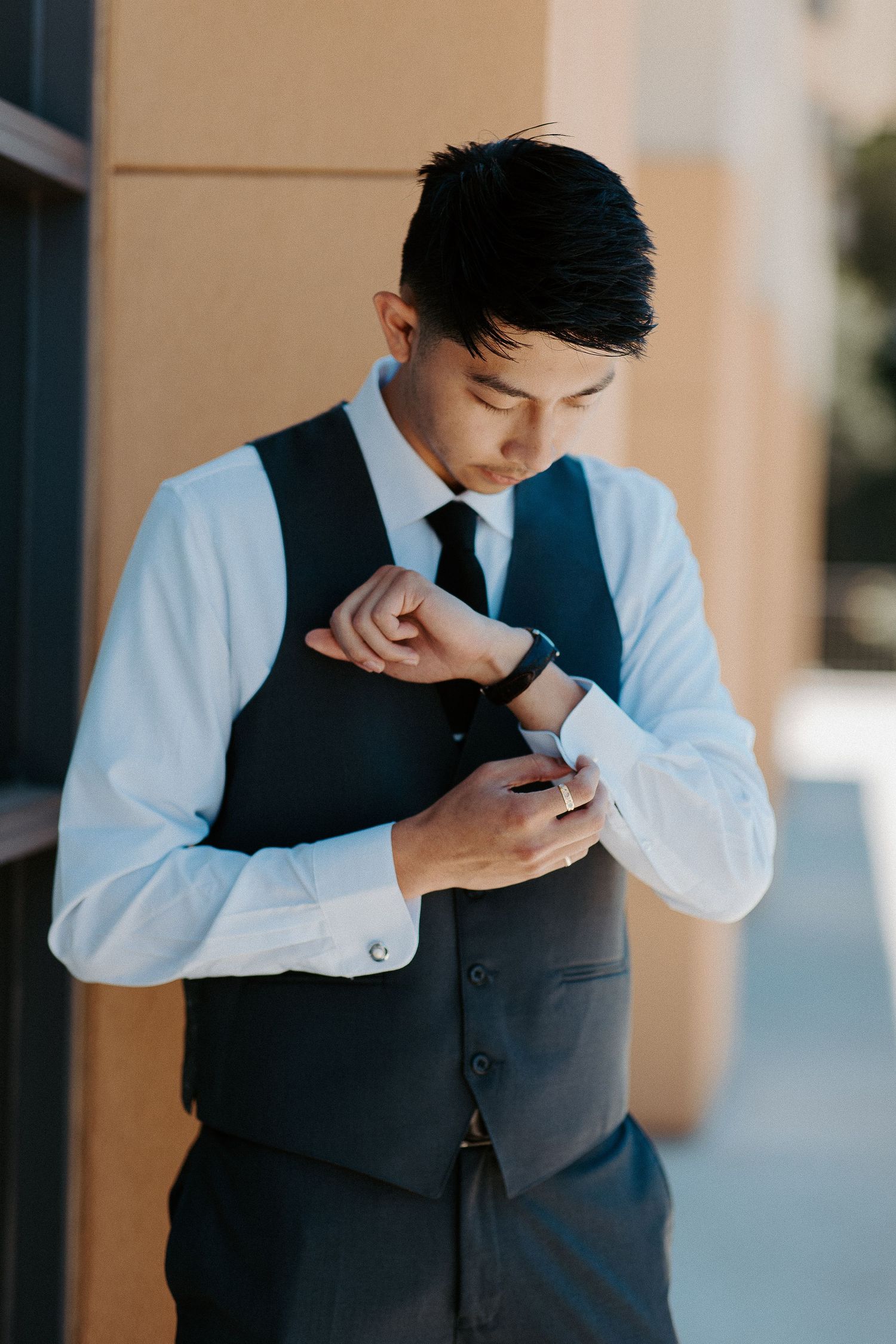 Professional in formal attire with white dress shirt and dark vest checks smartwatch while standing by a wall.