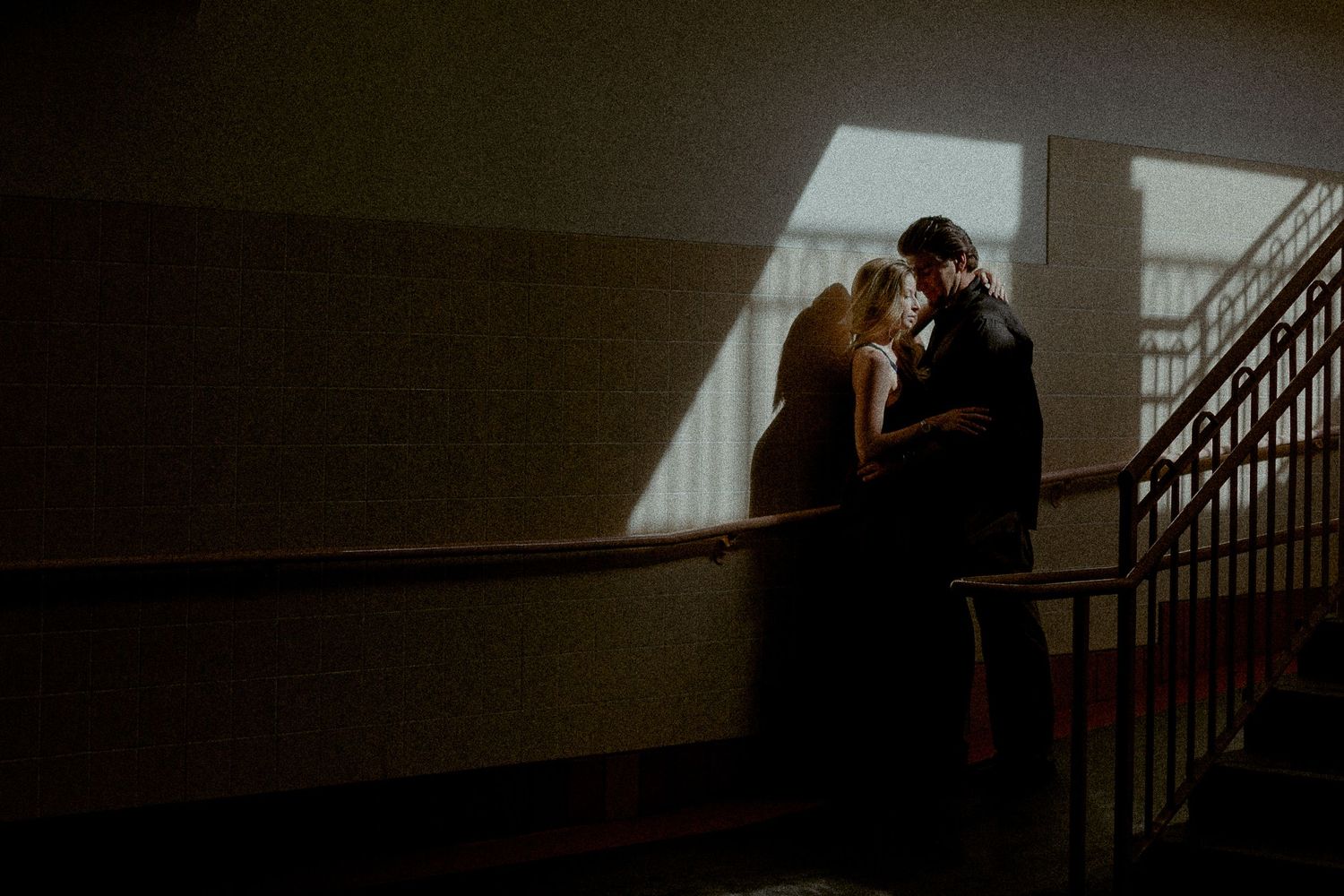 Silhouettes stand together in a dark hallway illuminated by dramatic window light.