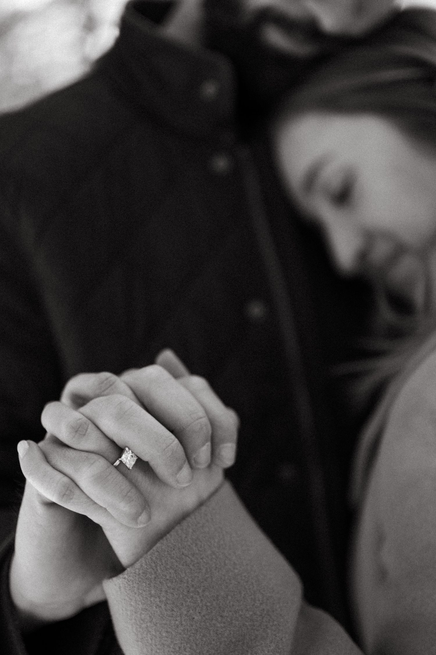 Close-up of clasped hands with an engagement ring in black and white.