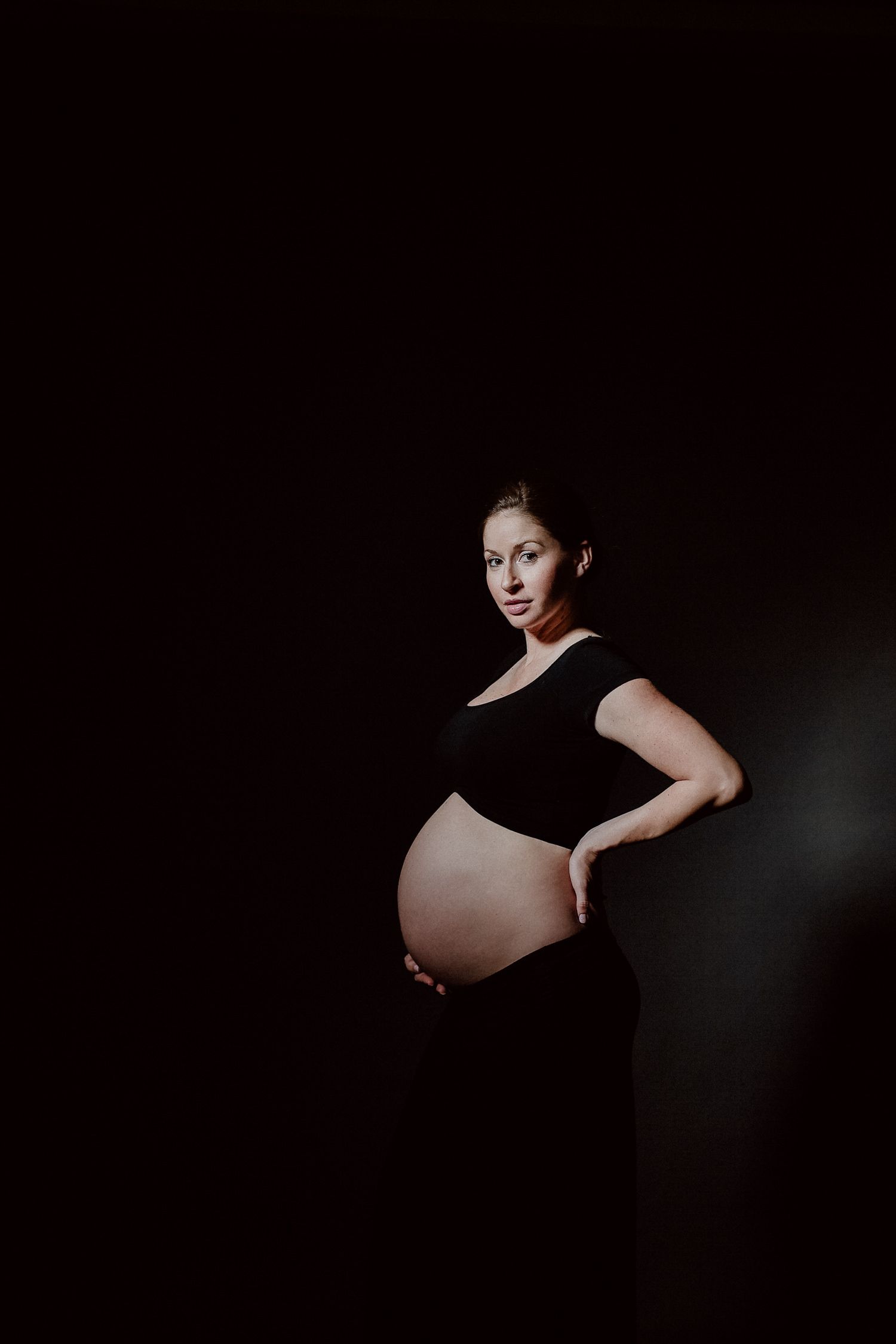Dramatic black and white maternity photo showing an expectant mother in dark room.