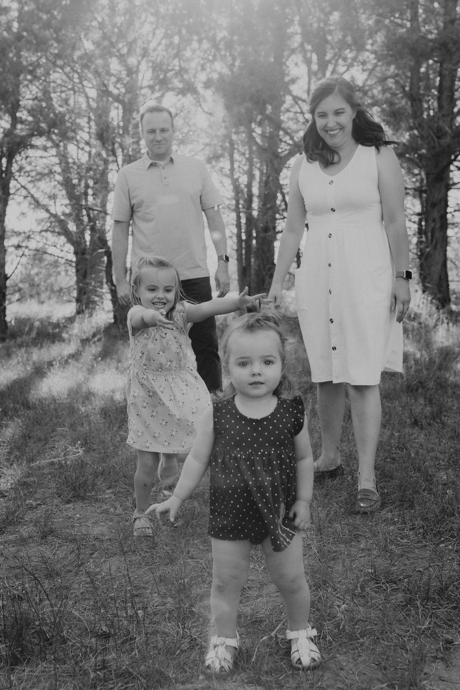 A black and white family portrait of four people standing outdoors among birch trees in a natural setting.