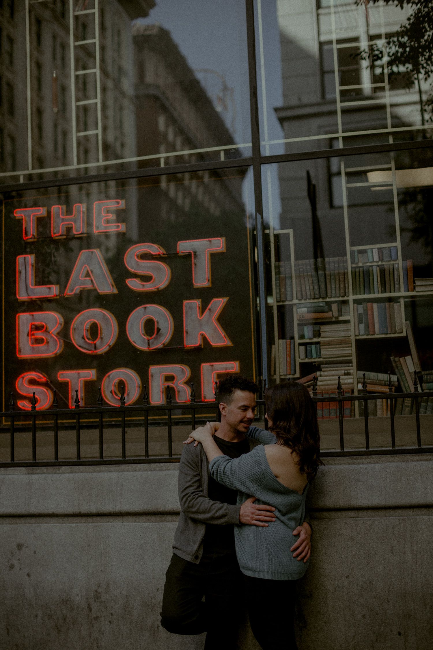 Couple embracing outside indie bookstore with red neon signage in urban setting.