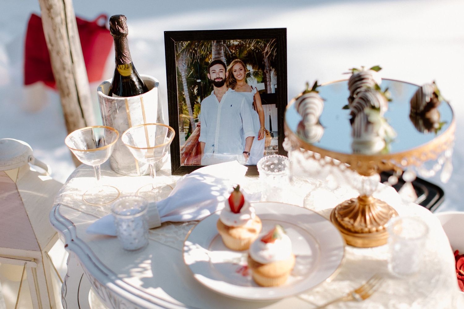 Romantic table setting with champagne, desserts and photos displayed in snowy outdoor setting.