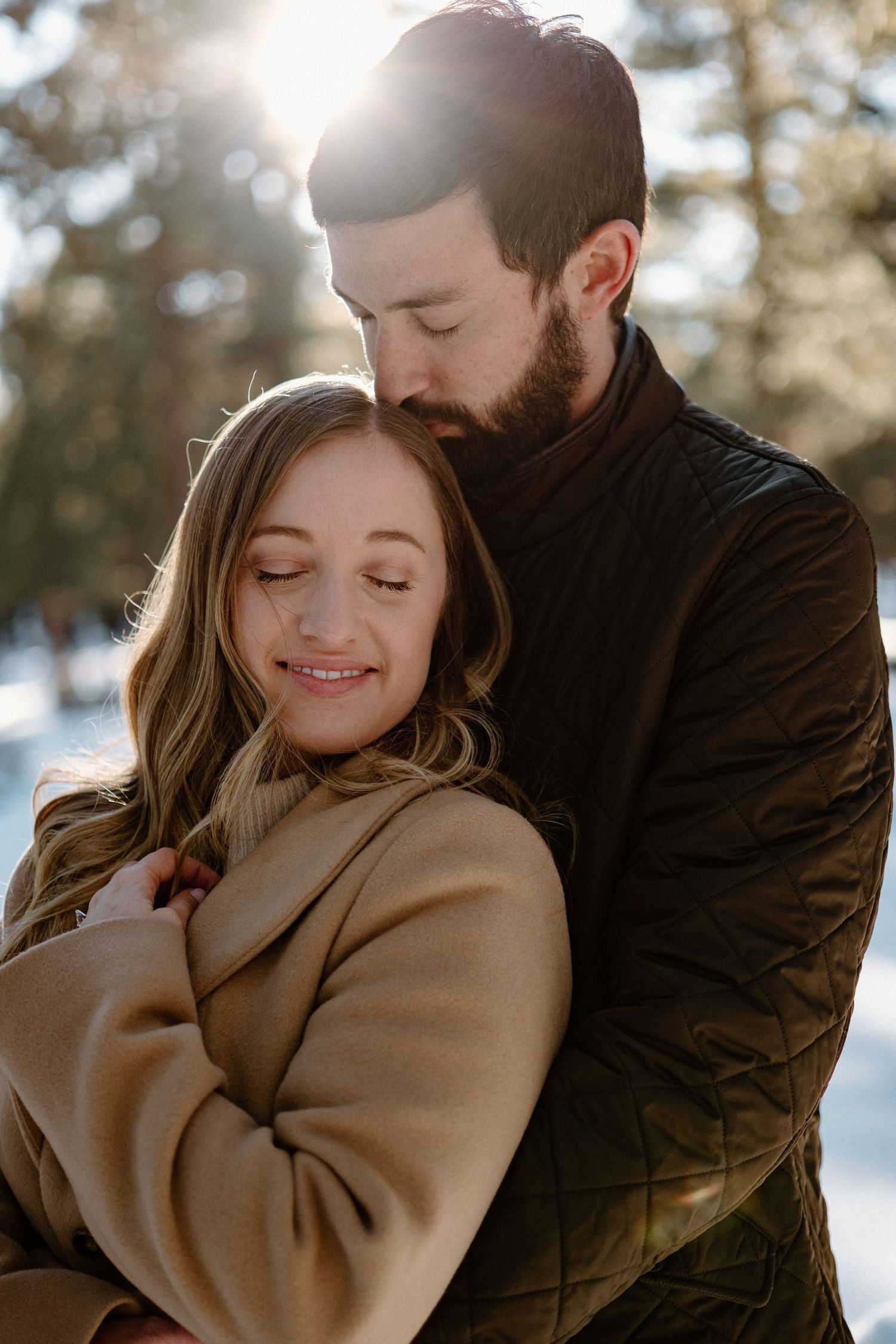 A tender winter embrace between a couple wearing warm coats in a snowy forest.