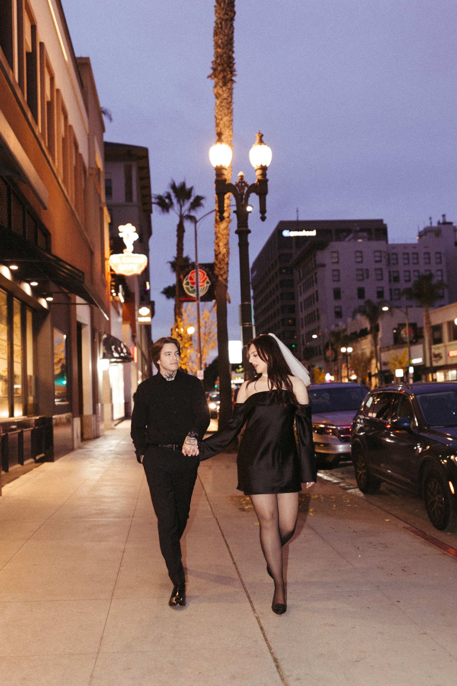 Couple strolling down illuminated urban sidewalk at dusk.