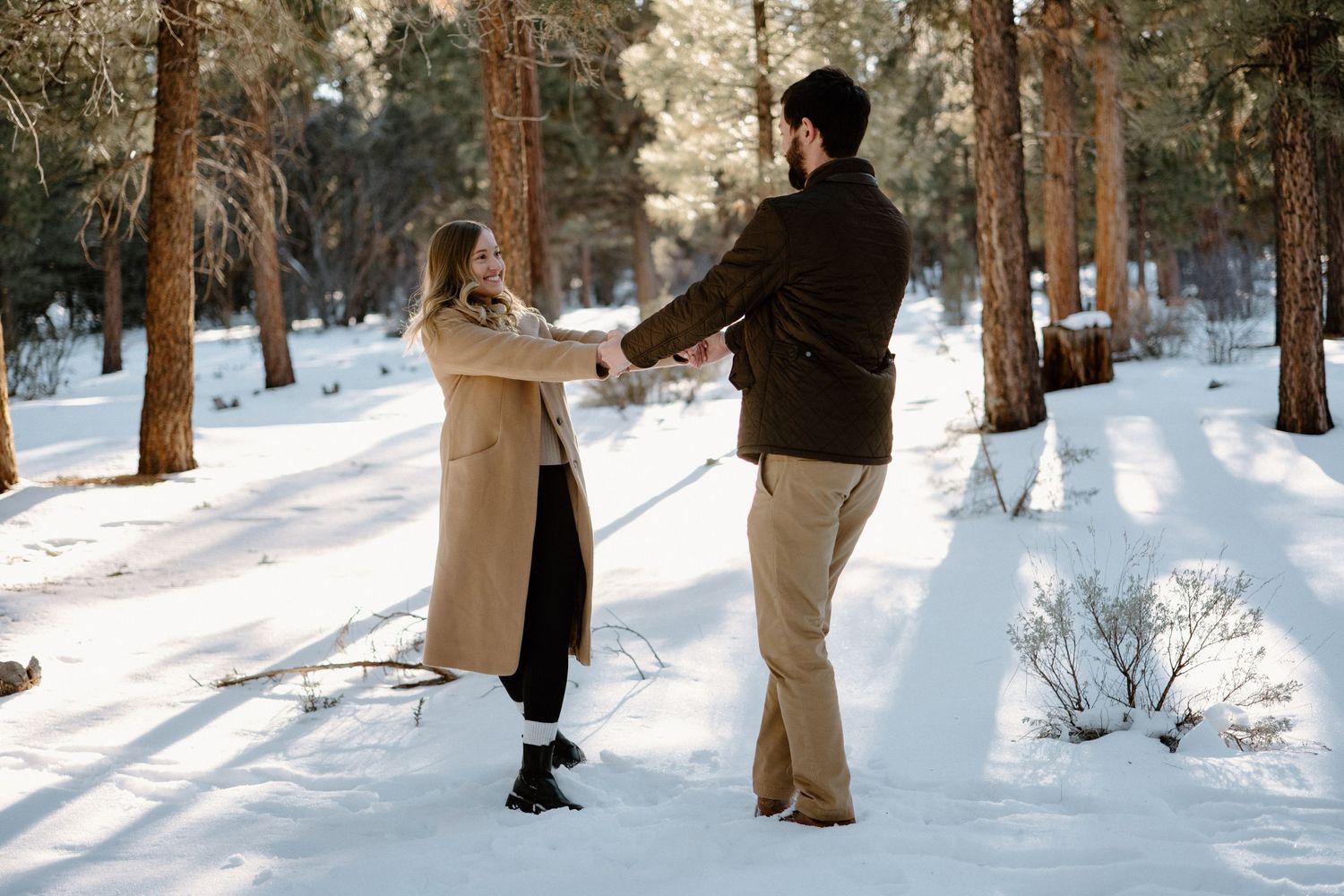 A couple dances together on a snow-covered path surrounded by pine trees.