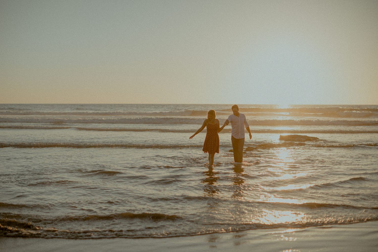 Two people wading together in shallow ocean waters during a beautiful sunset.