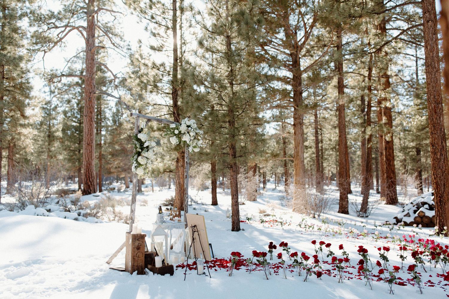 Intimate winter forest setting with table decorated with red rose petals in snow.