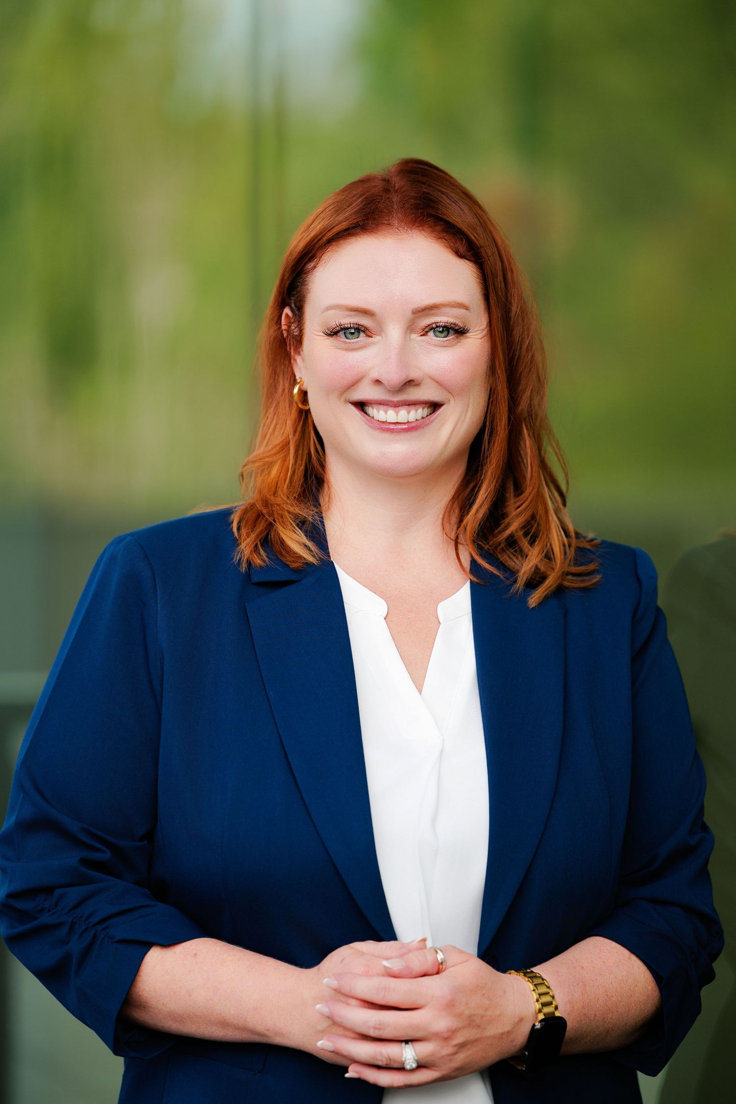 Professional headshot series showing a person in a navy blazer and white shirt against a blurred green natural backdrop.