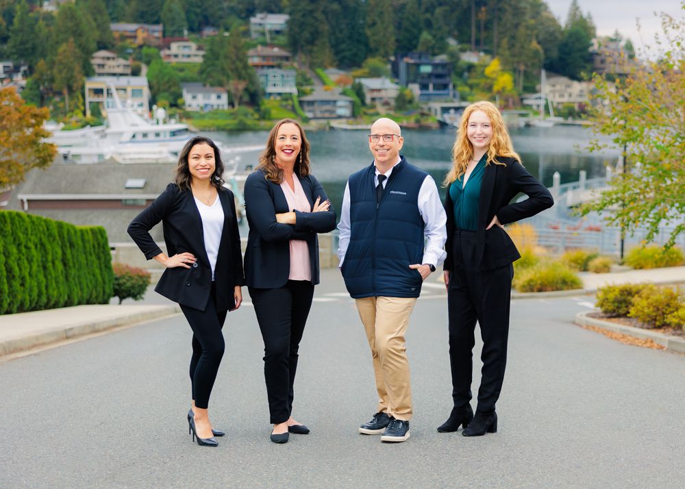 Four professionals in business attire pose on street with waterfront view.