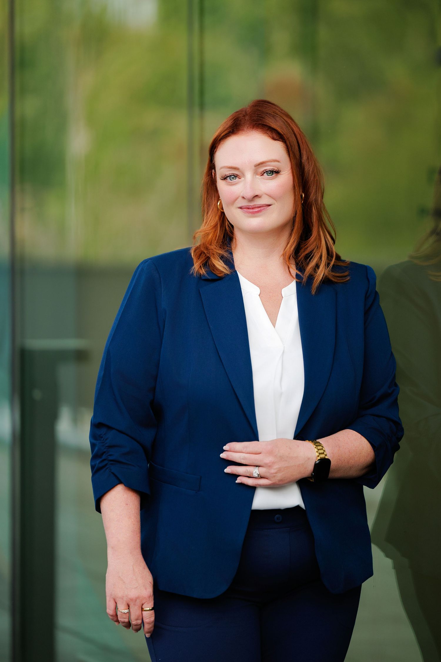Professional business portrait in navy blazer and white blouse against blurred green background.