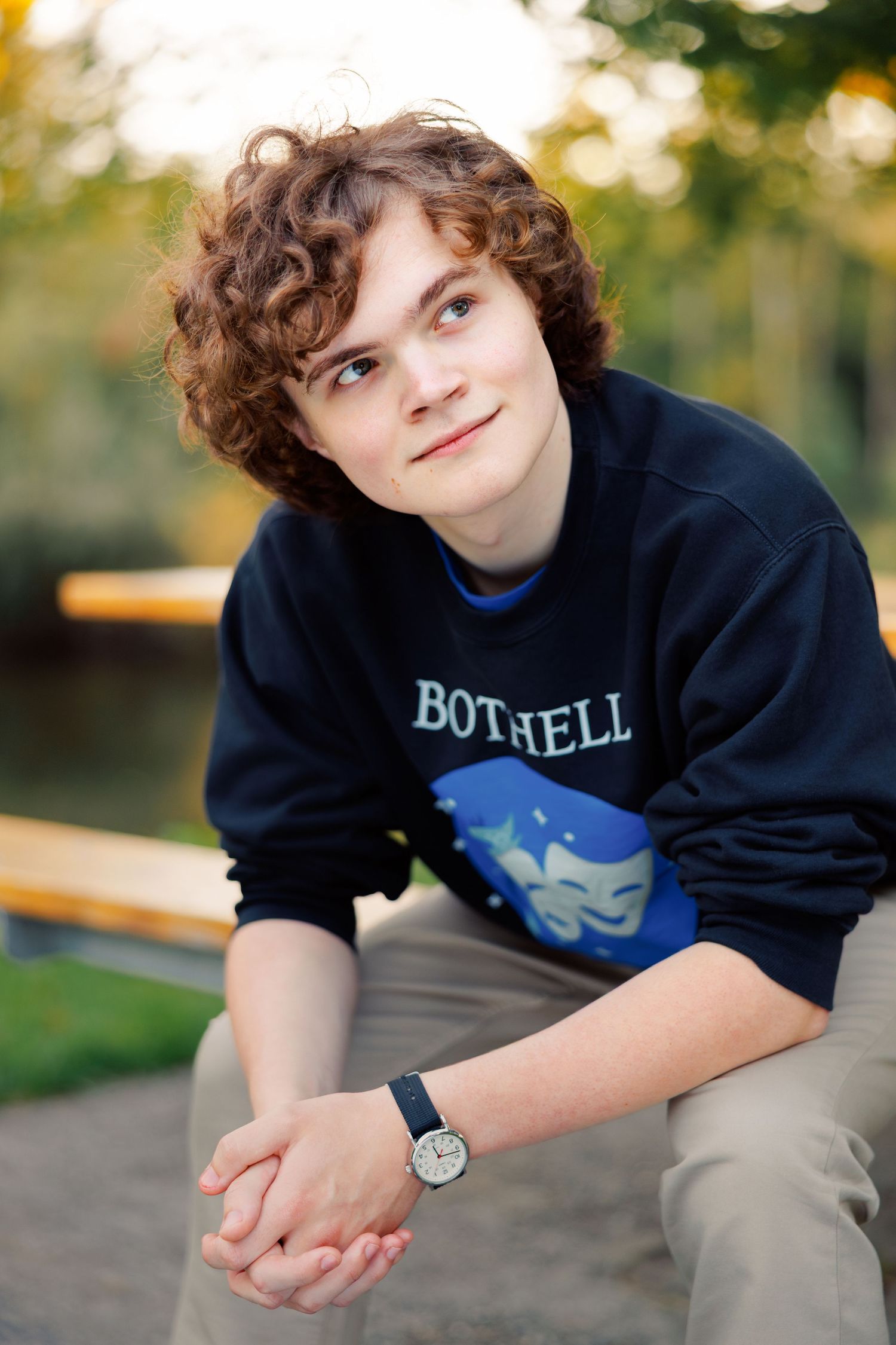 A person wearing a navy blue Bothell sweatshirt poses casually outdoors during golden hour.