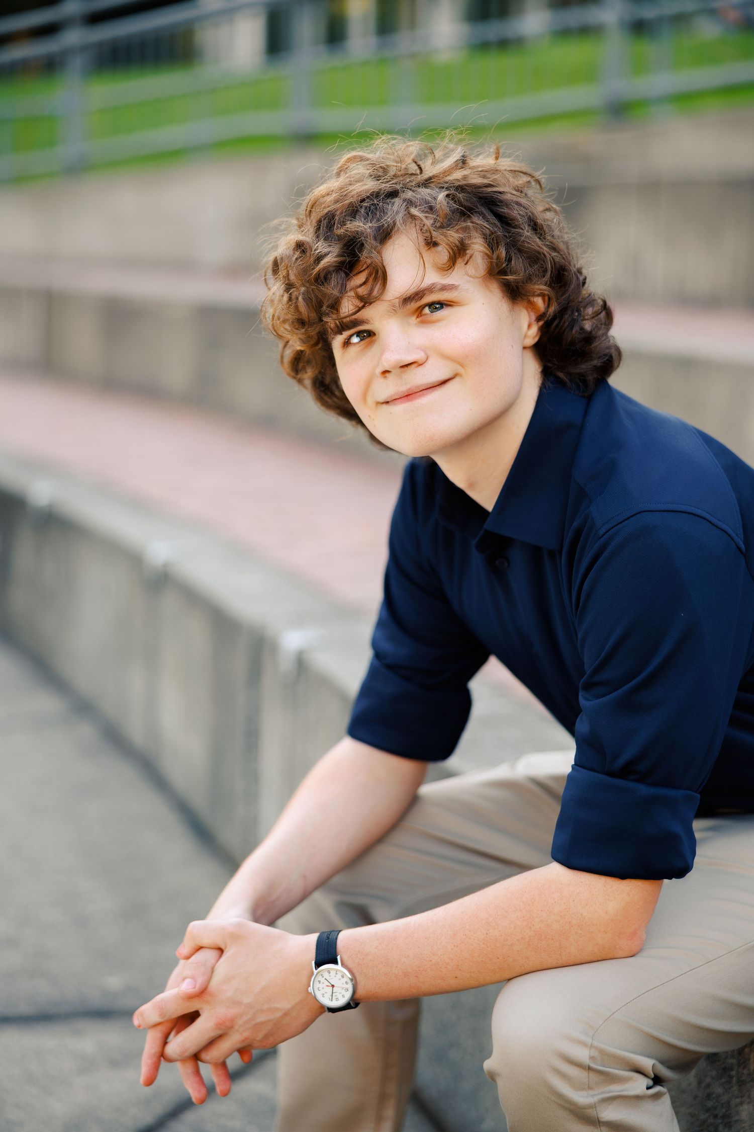 Person wearing a navy polo shirt sits casually on concrete steps outdoors.
