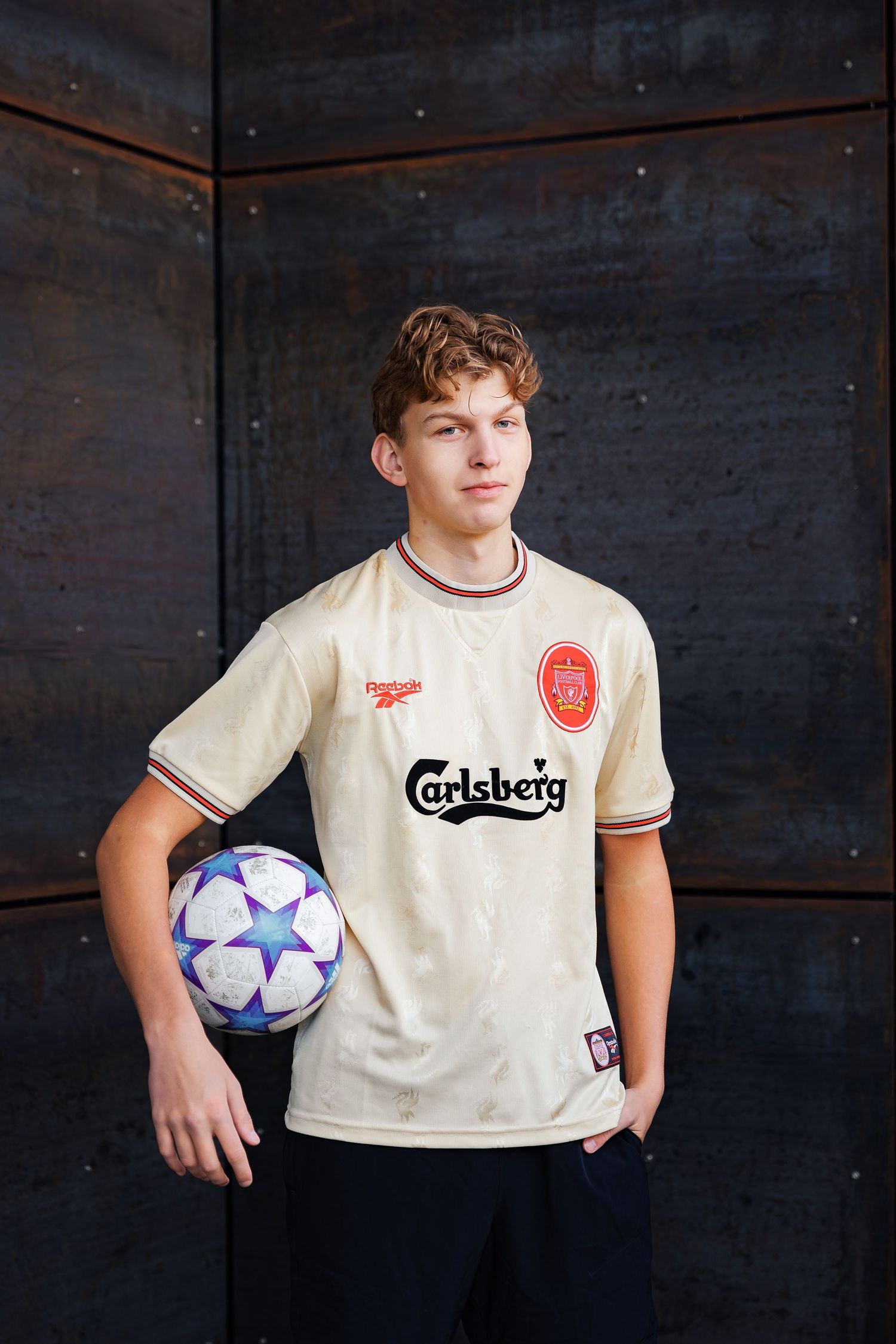 A vintage Liverpool FC jersey with Carlsberg sponsor displayed in dark moody lighting with soccer ball.
